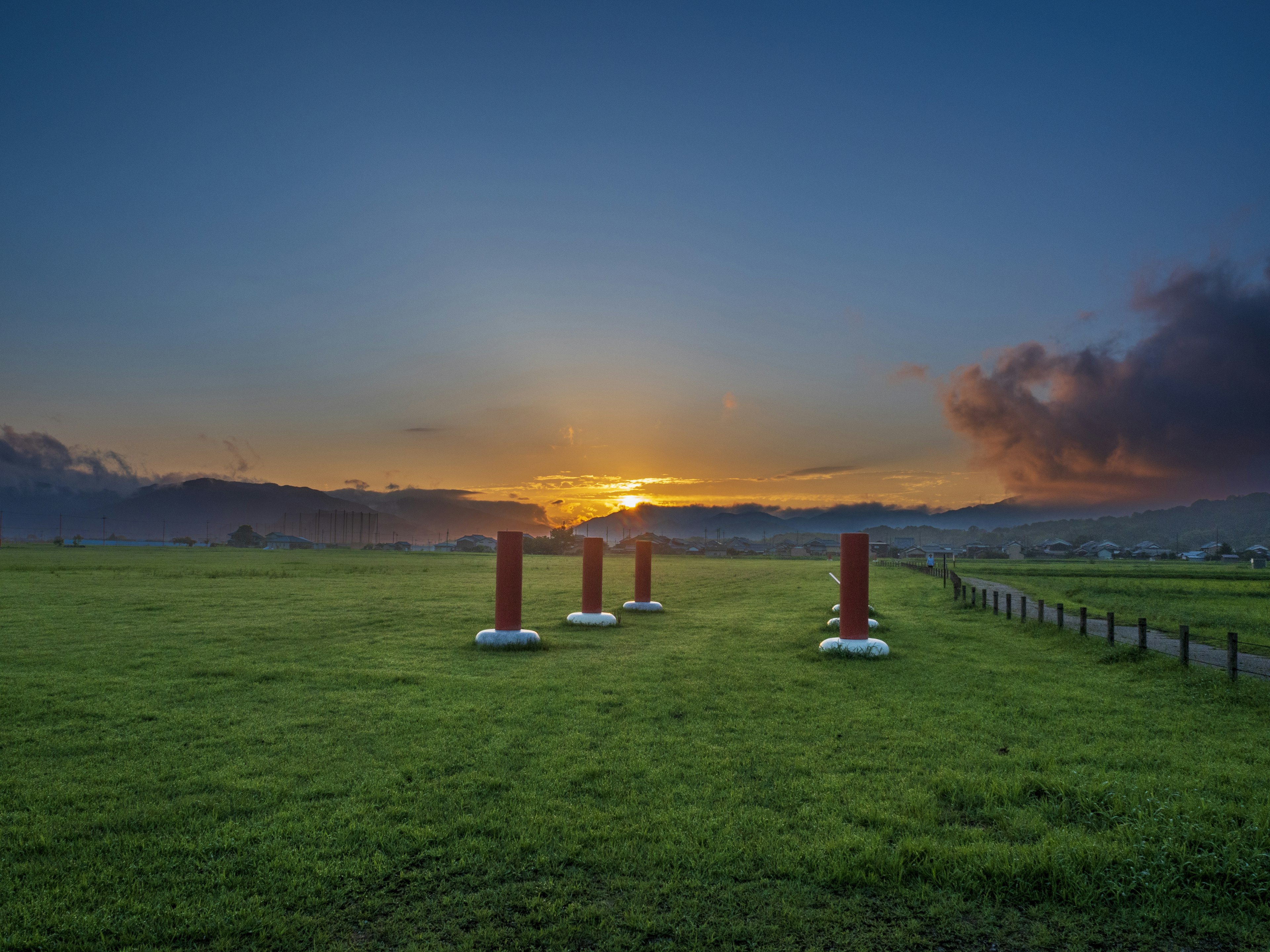 Red pillars in a green field at sunset