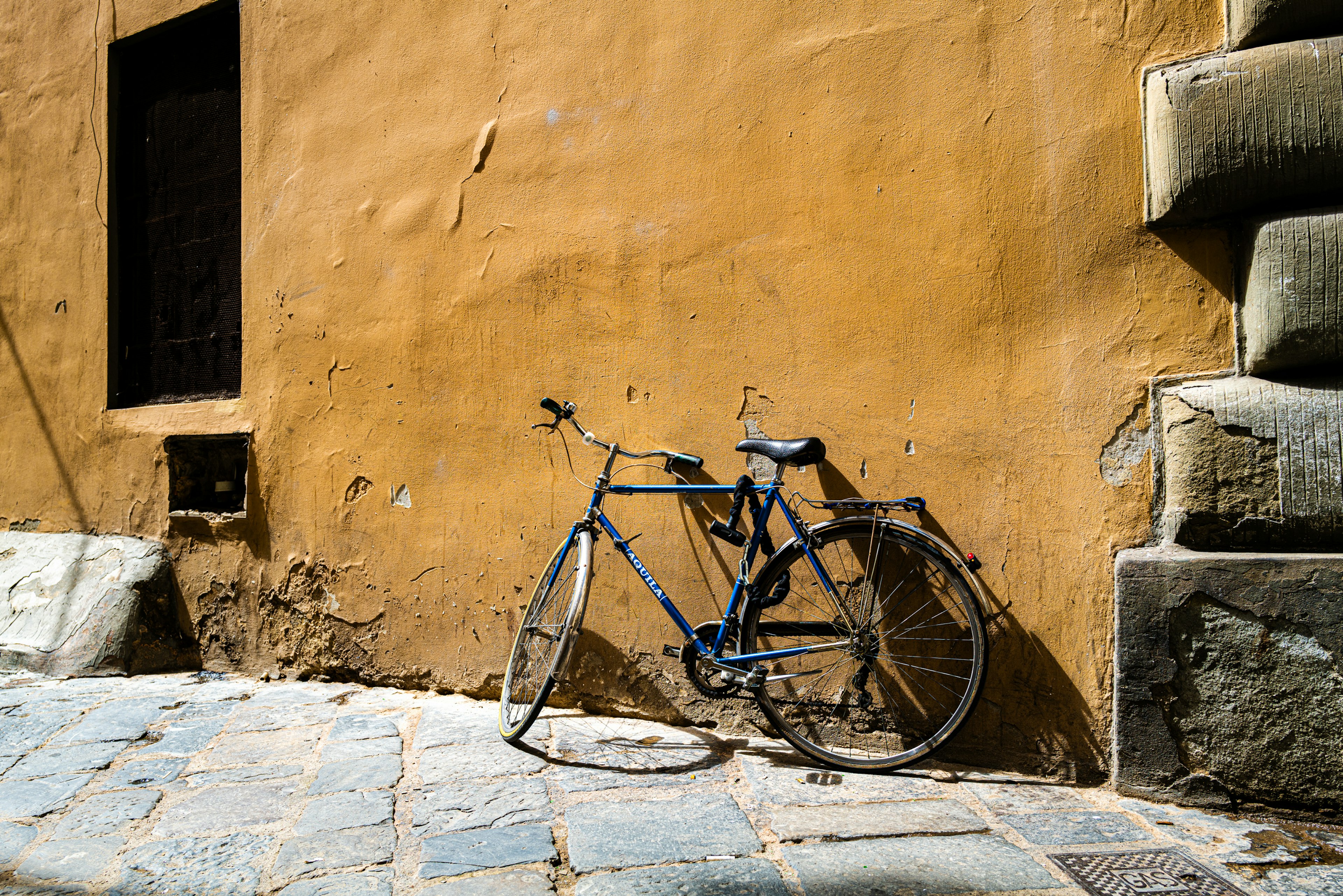 Una vecchia bicicletta blu appoggiata a un muro arancione