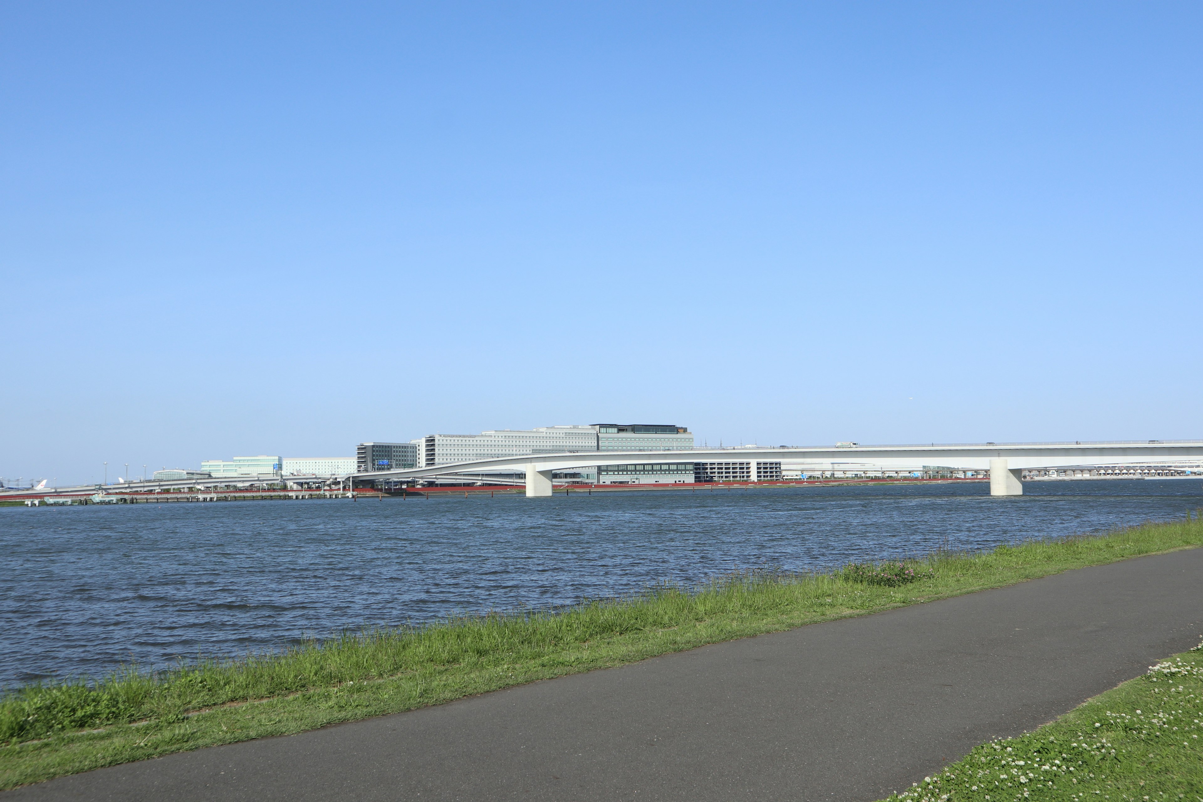 Scenic view of a river with a walking path and buildings in the distance under a clear blue sky