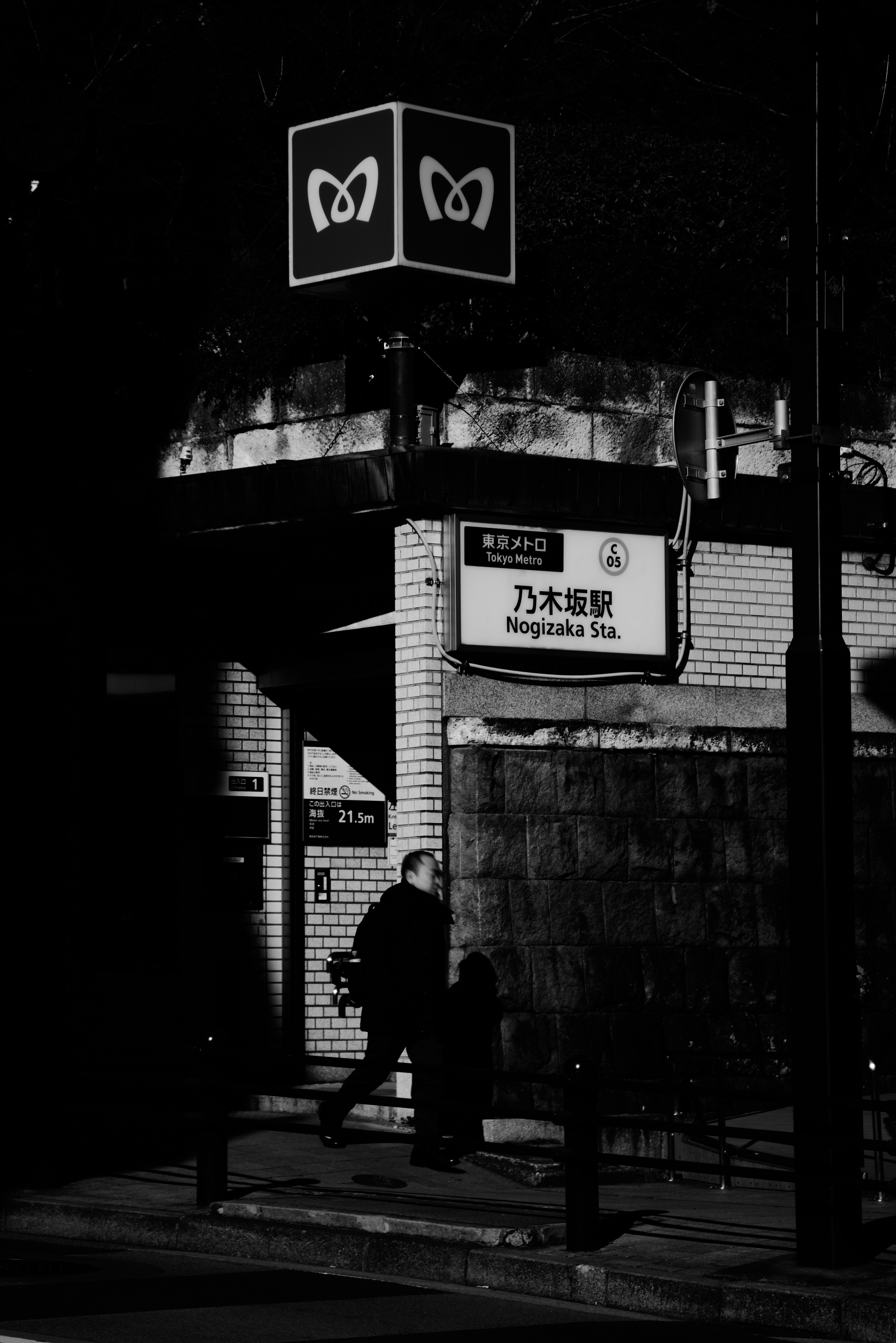 Scène de rue en noir et blanc avec une personne marchant et un panneau bien visible