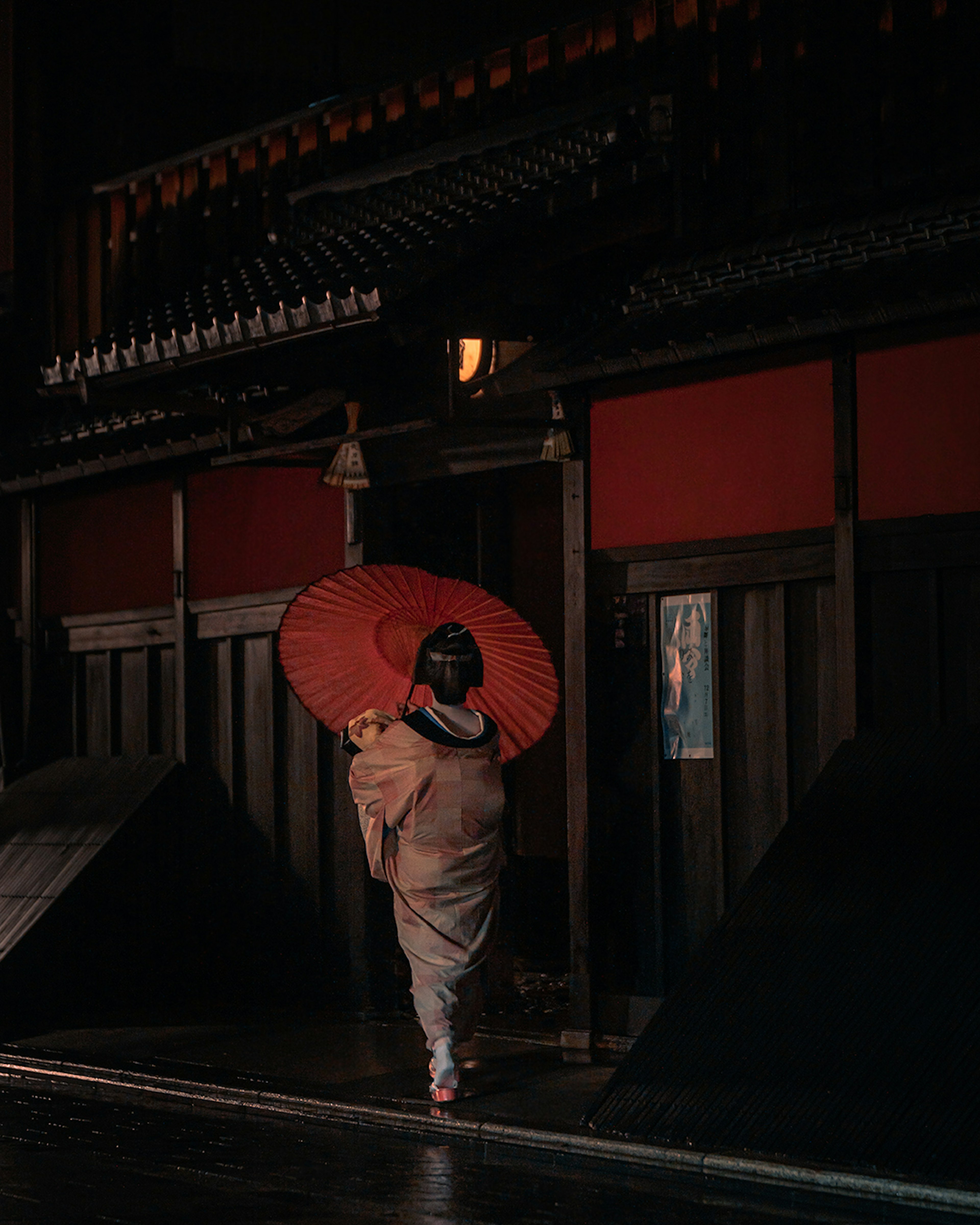 Una donna in kimono con un ombrello rosso cammina davanti a un edificio giapponese tradizionale