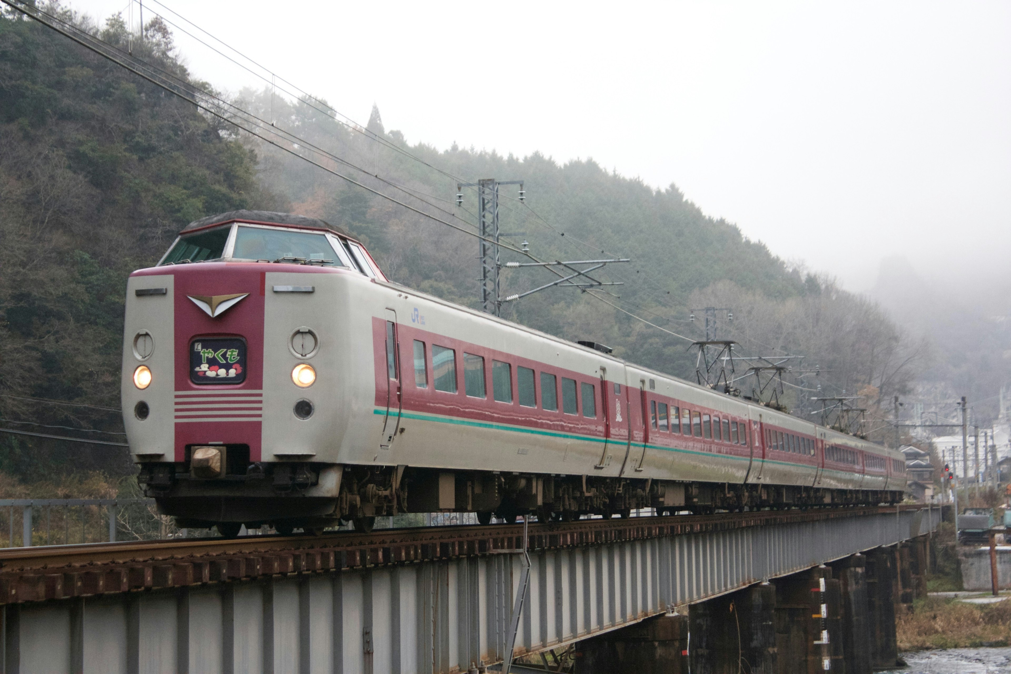 Tren exprés con rayas rojas cruzando un puente en una zona montañosa