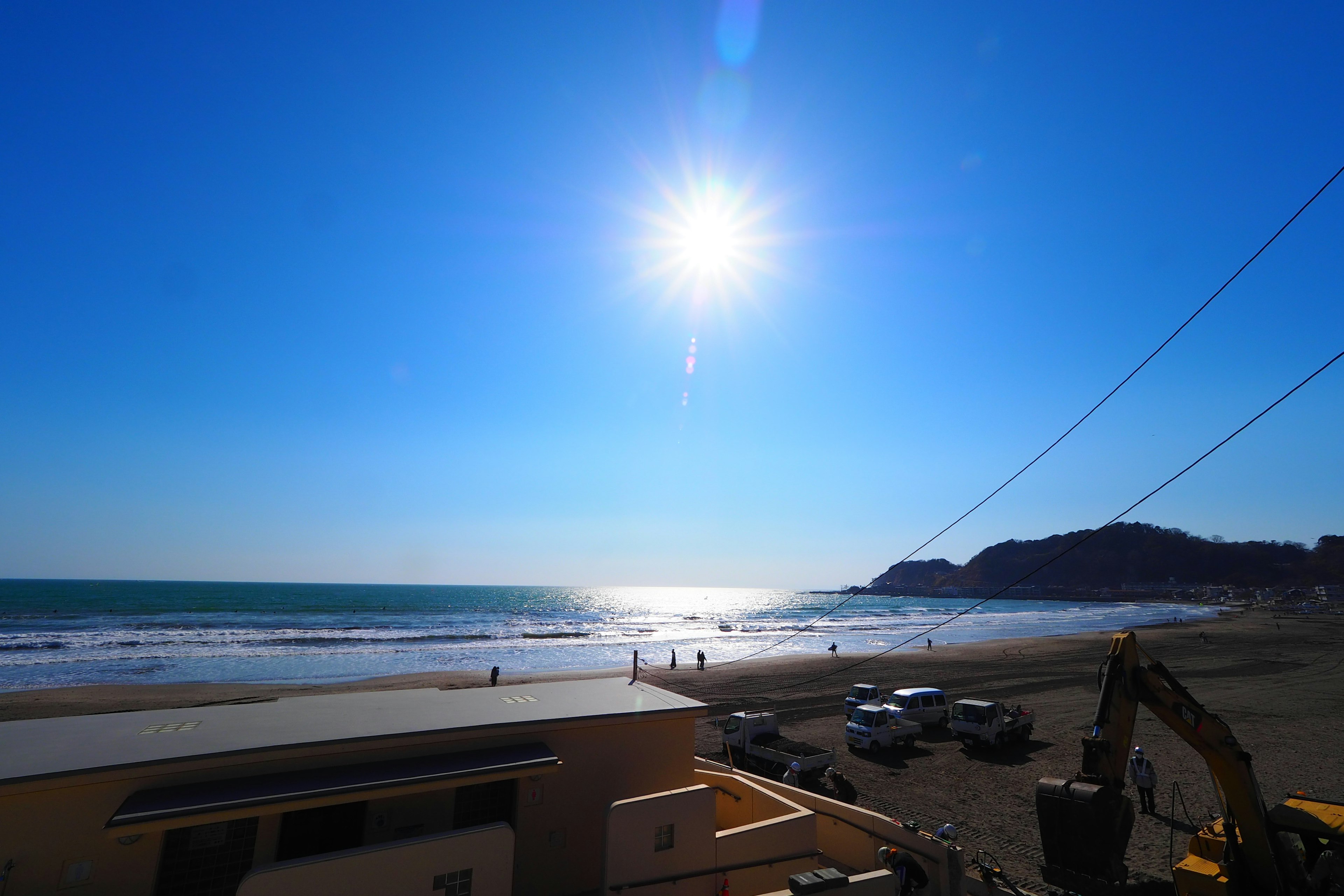 Coastal scene with bright sun over the ocean waves and sandy beach visible under a clear blue sky