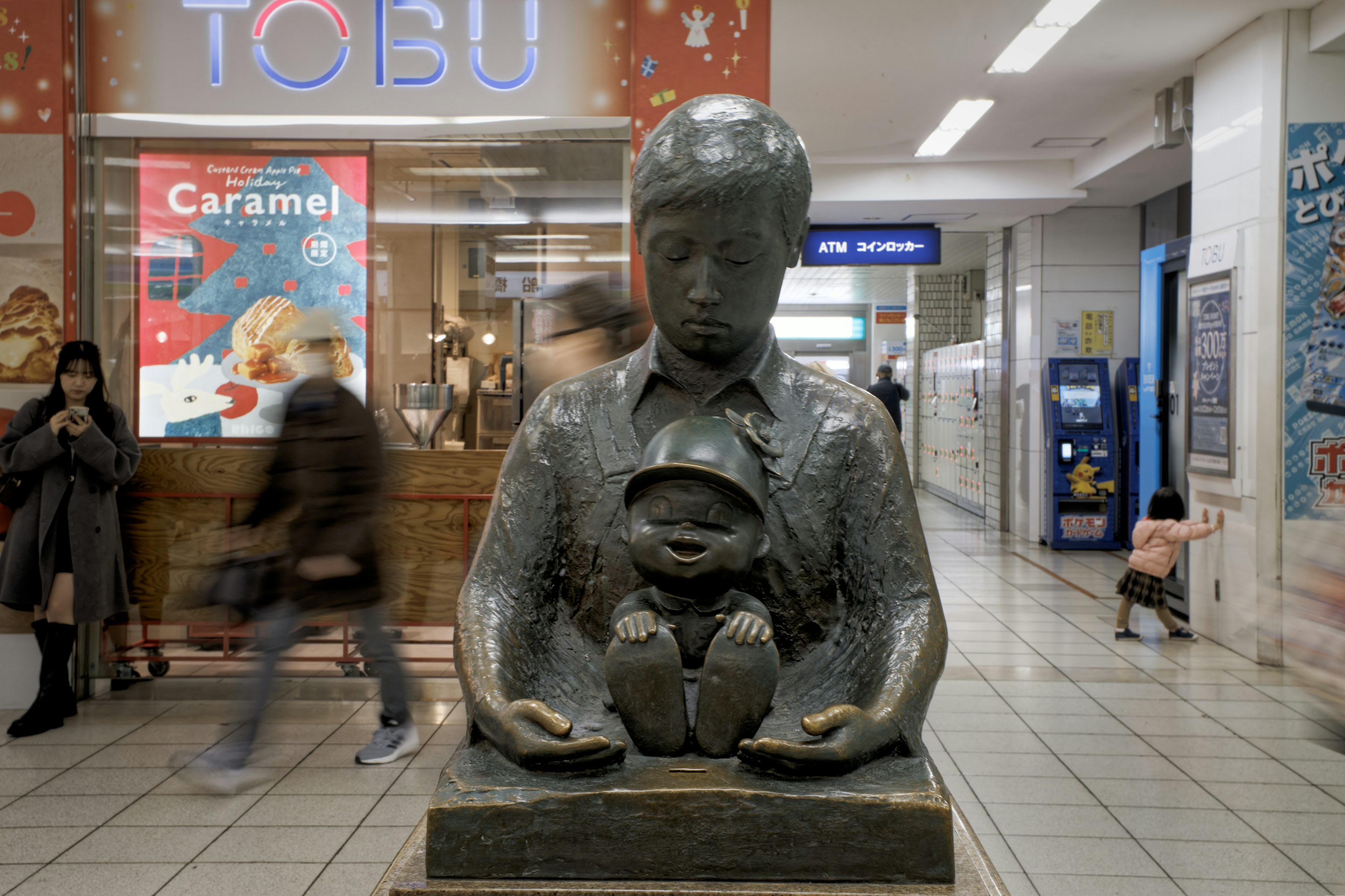 Une statue d'un garçon tenant un enfant devant un magasin TOBU