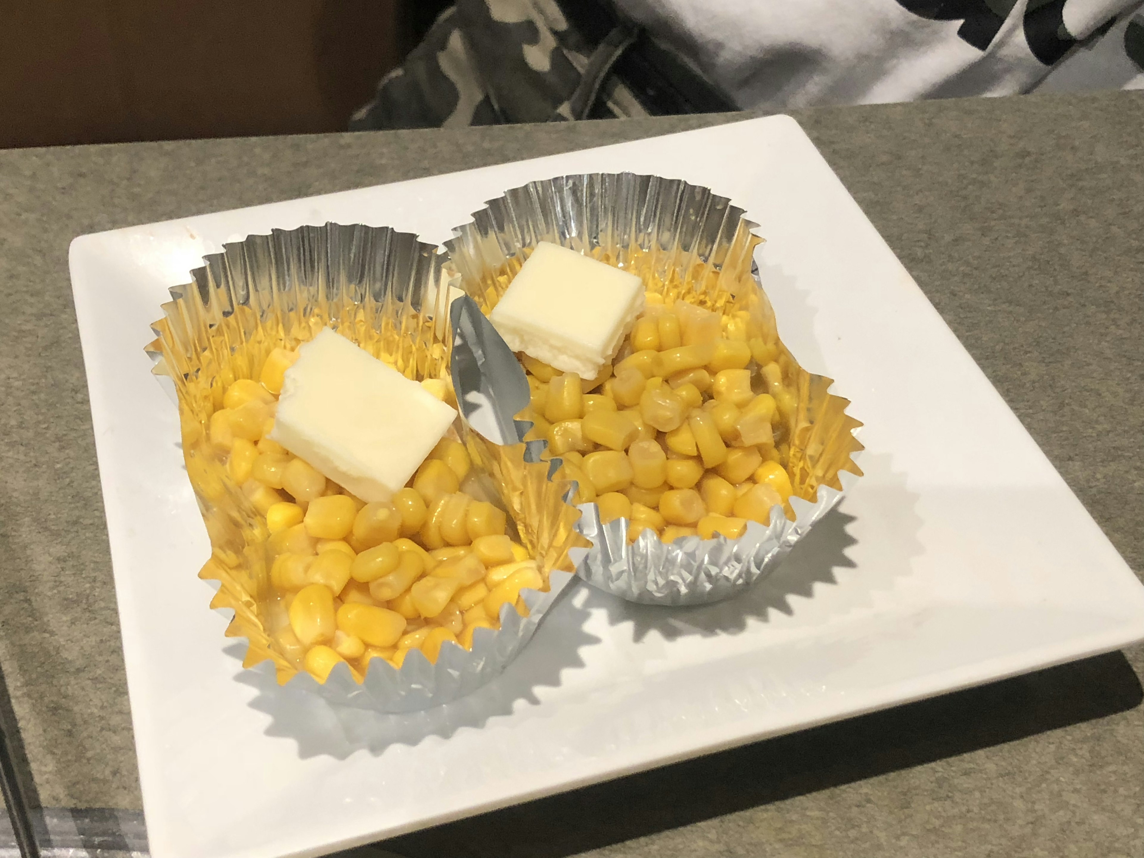 Two aluminum cups filled with yellow corn topped with butter