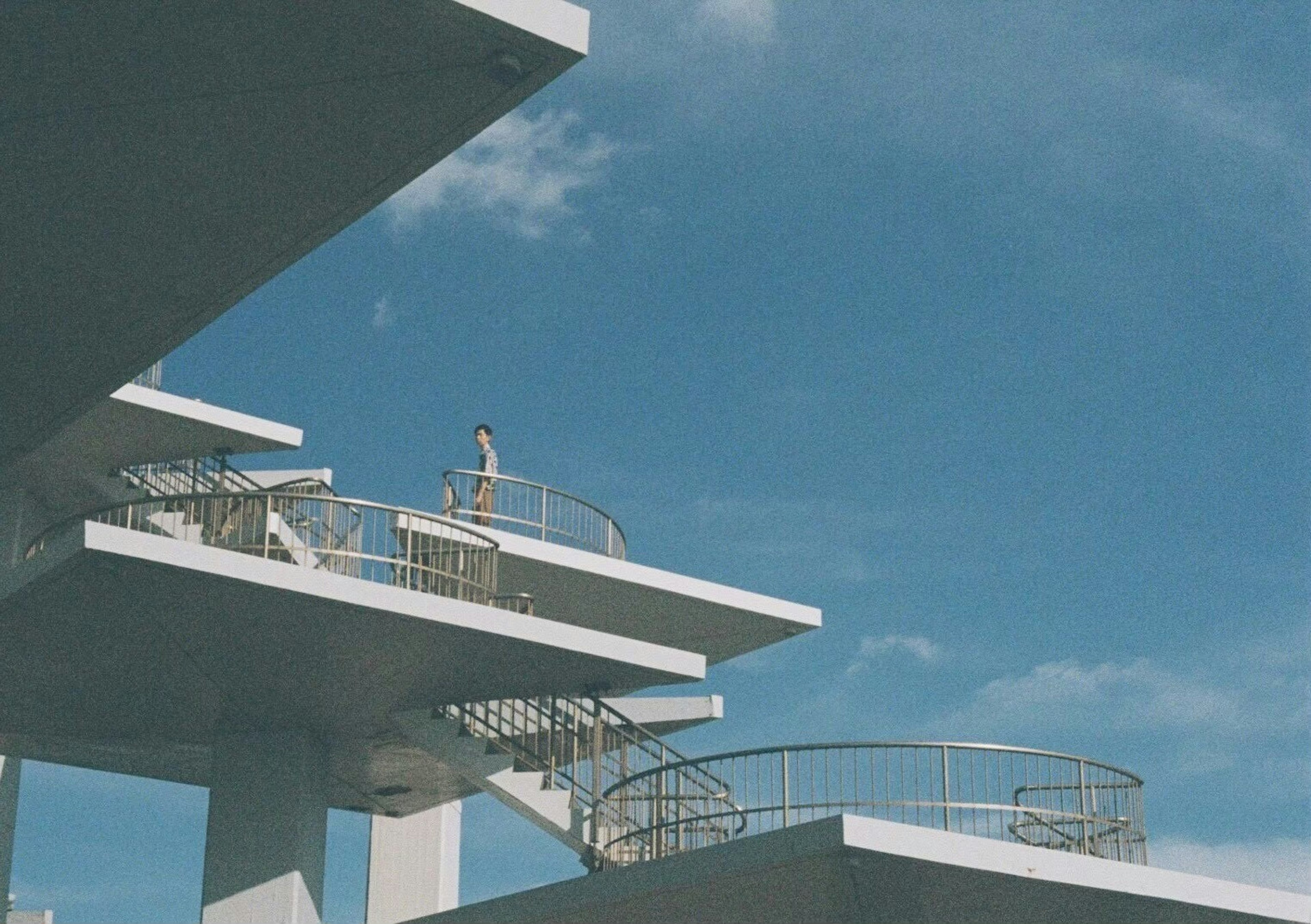 Un edificio moderno con escaleras bajo un cielo azul y una persona subiendo