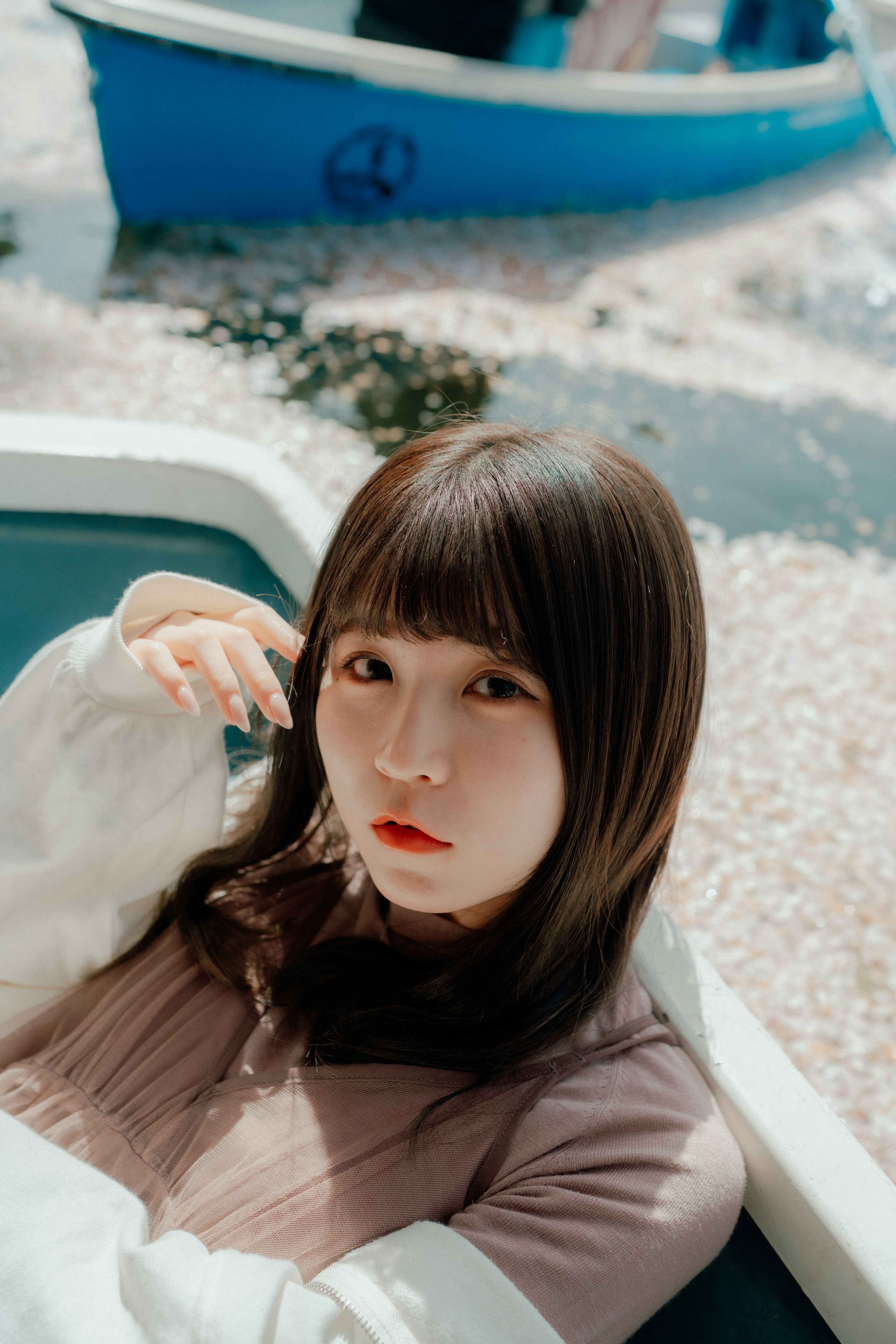 A young woman sitting in a boat surrounded by cherry blossom petals