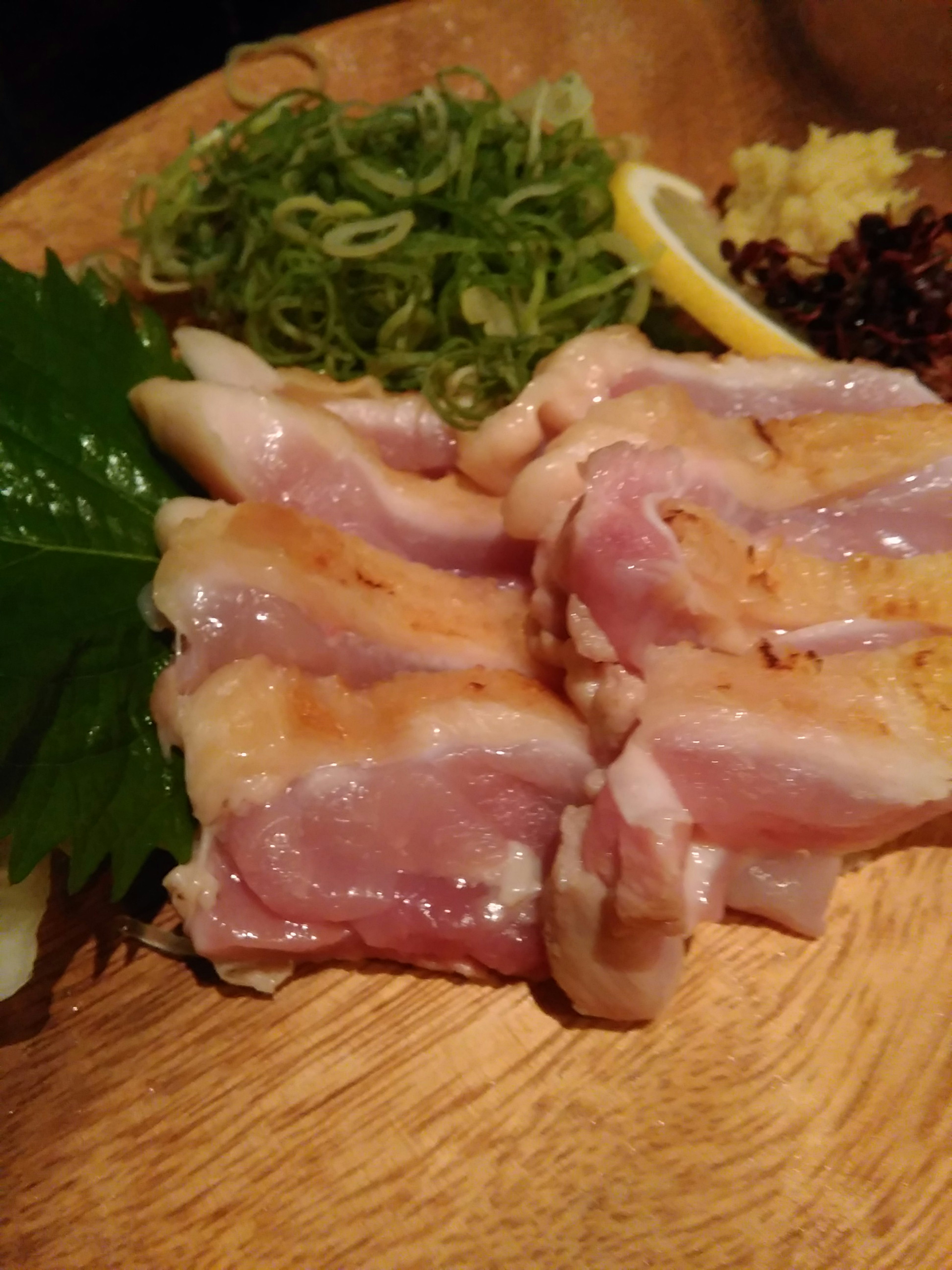 Pollo fresco en rodajas sobre un plato de madera con cebollas verdes y limón