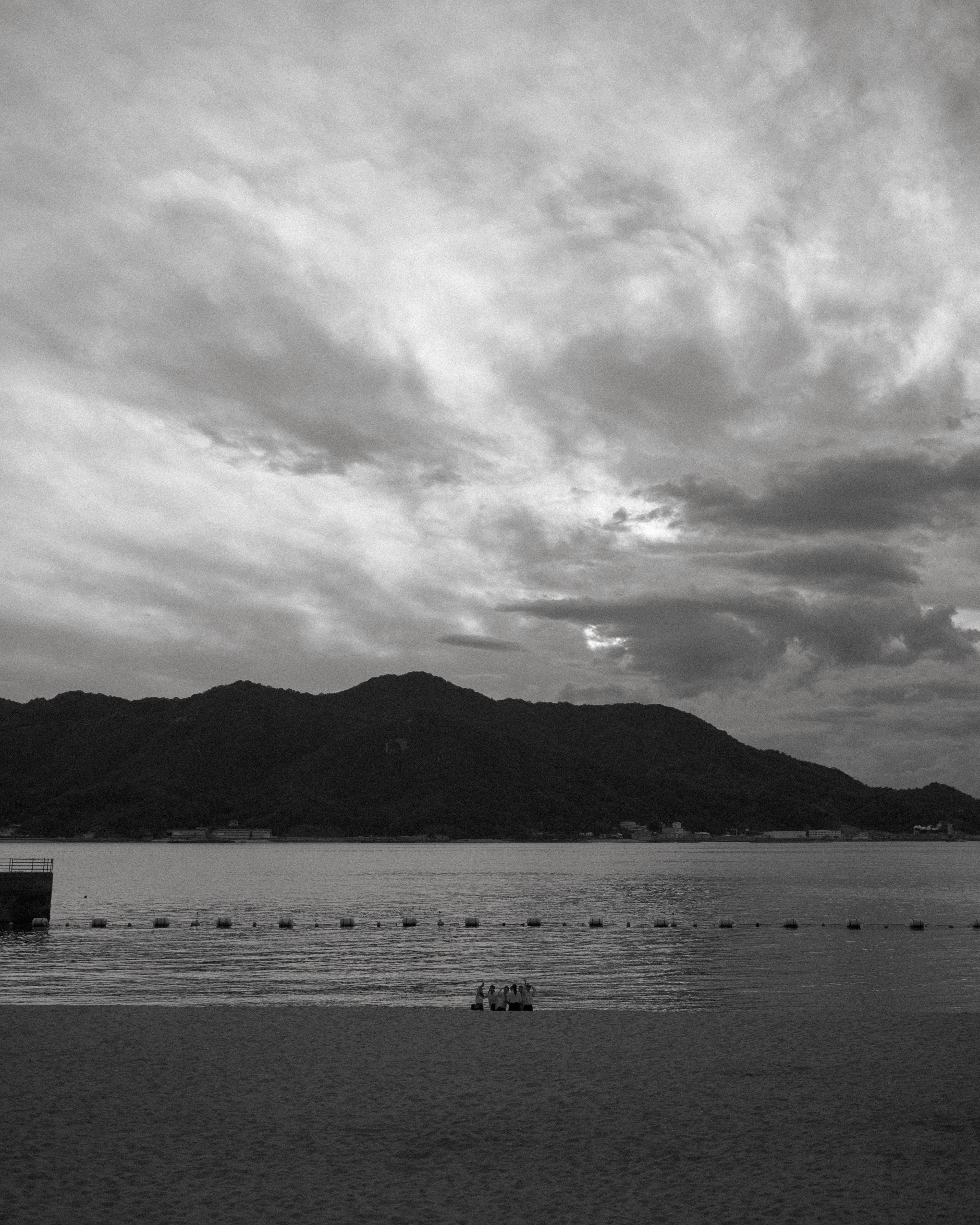 Black and white image of a beach with mountains and cloudy sky