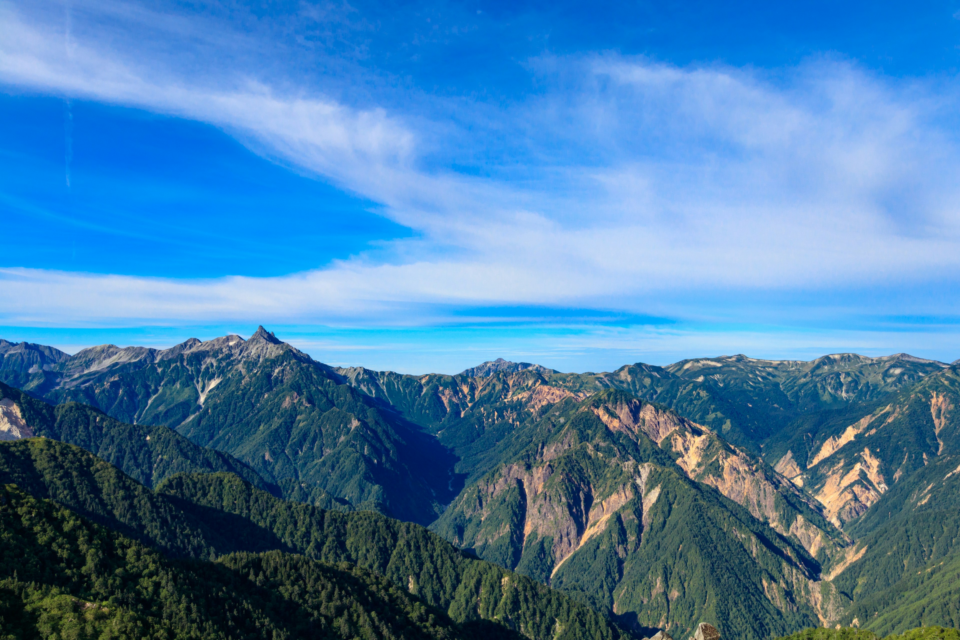 Pemandangan megah pegunungan di bawah langit biru vegetasi subur dan puncak berbatu