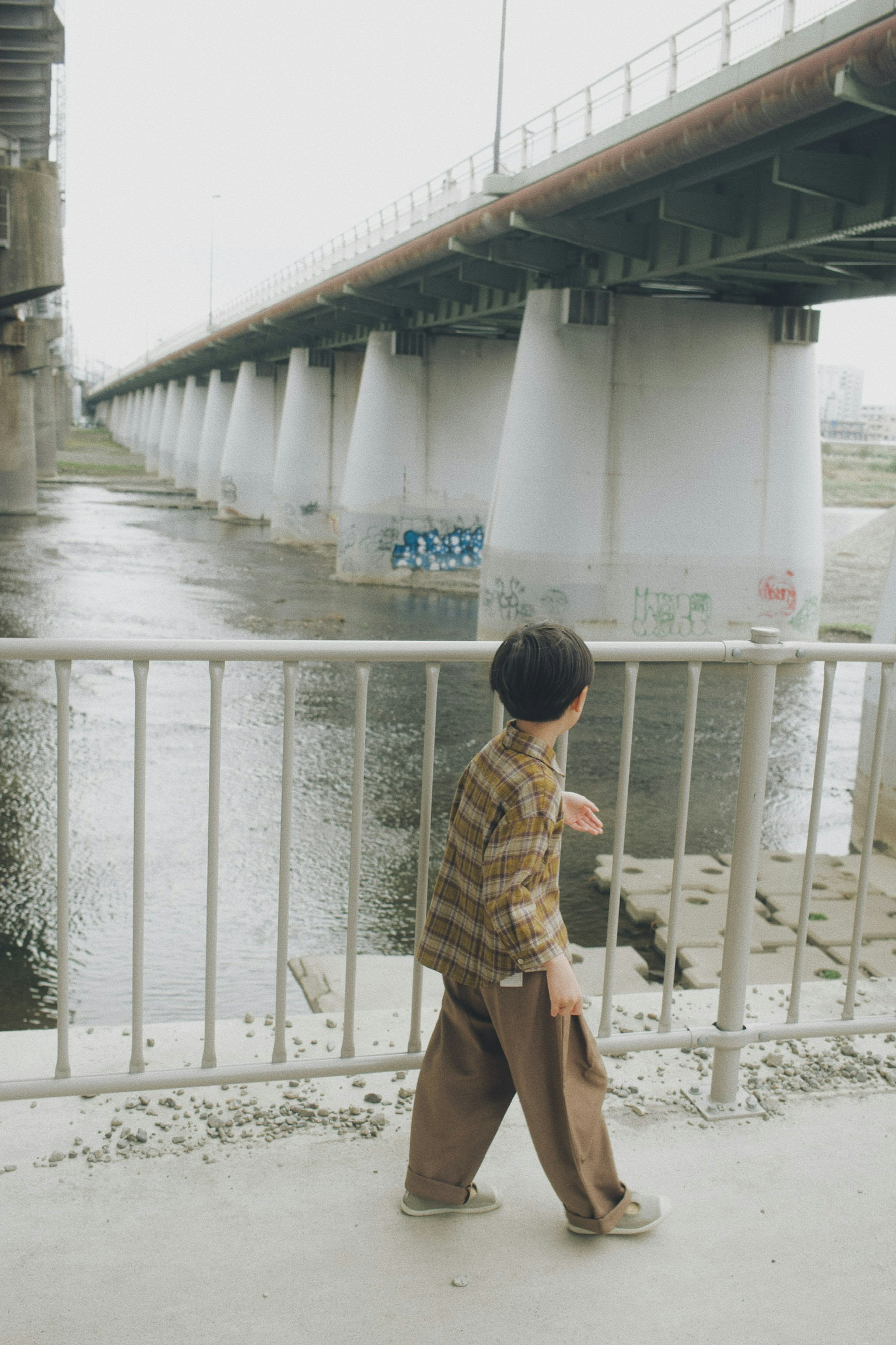 Kind, das entlang eines Flussufers unter einer Brücke mit ruhigem Wasser geht