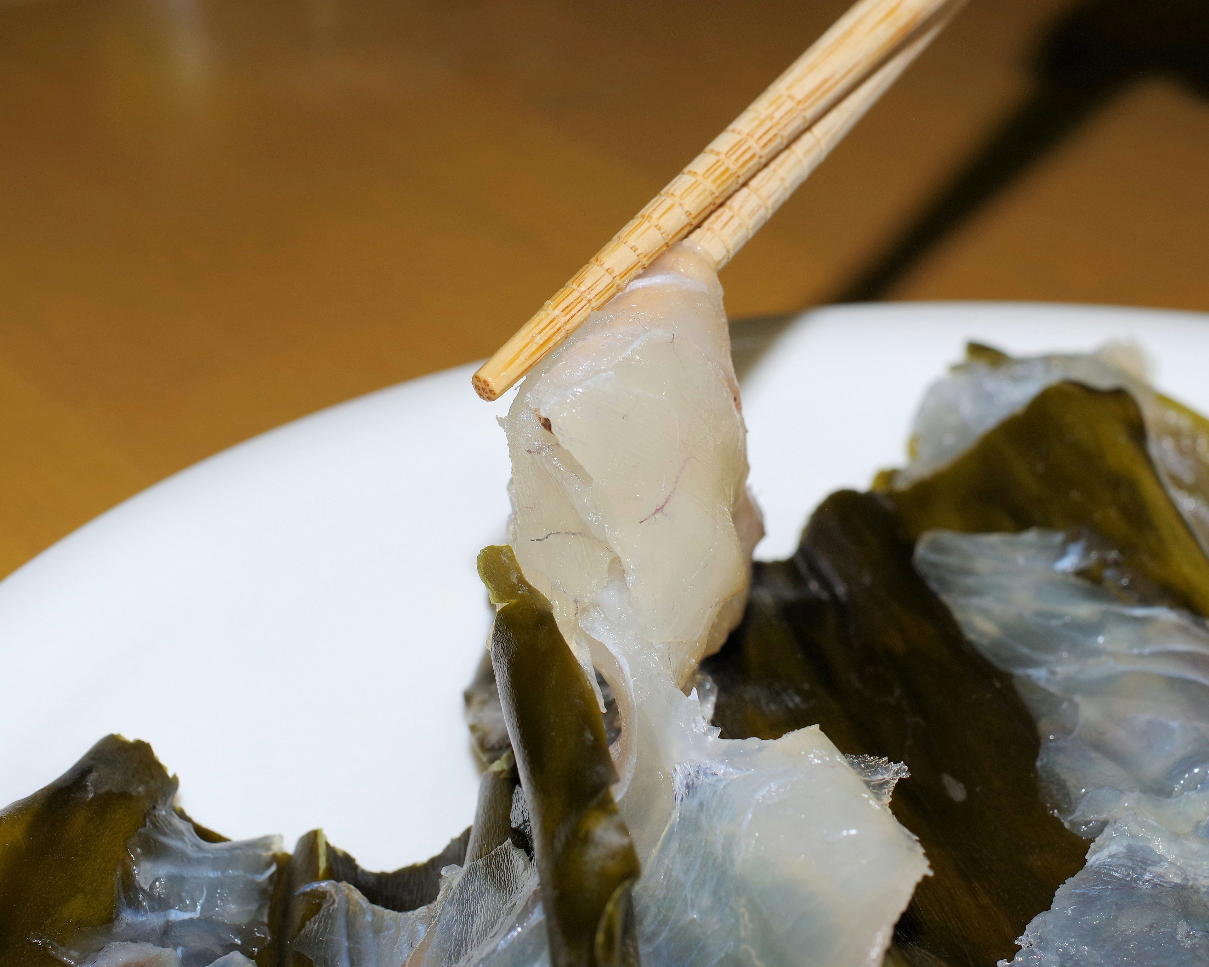 Un morceau de poisson translucide tenu avec des baguettes sur des algues