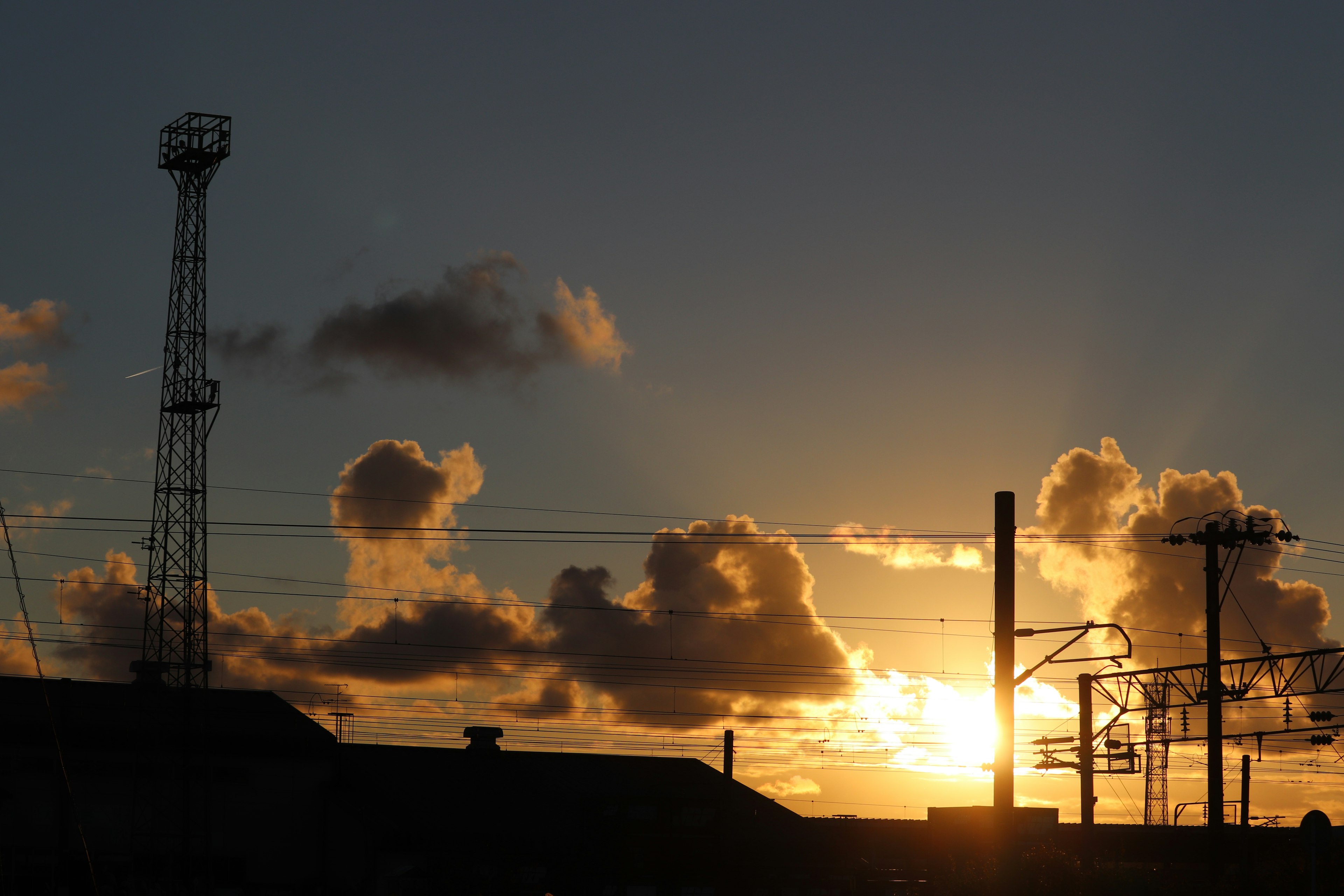 Silhouette di un paesaggio industriale al tramonto con linee ferroviarie aeree e una torre di comunicazione