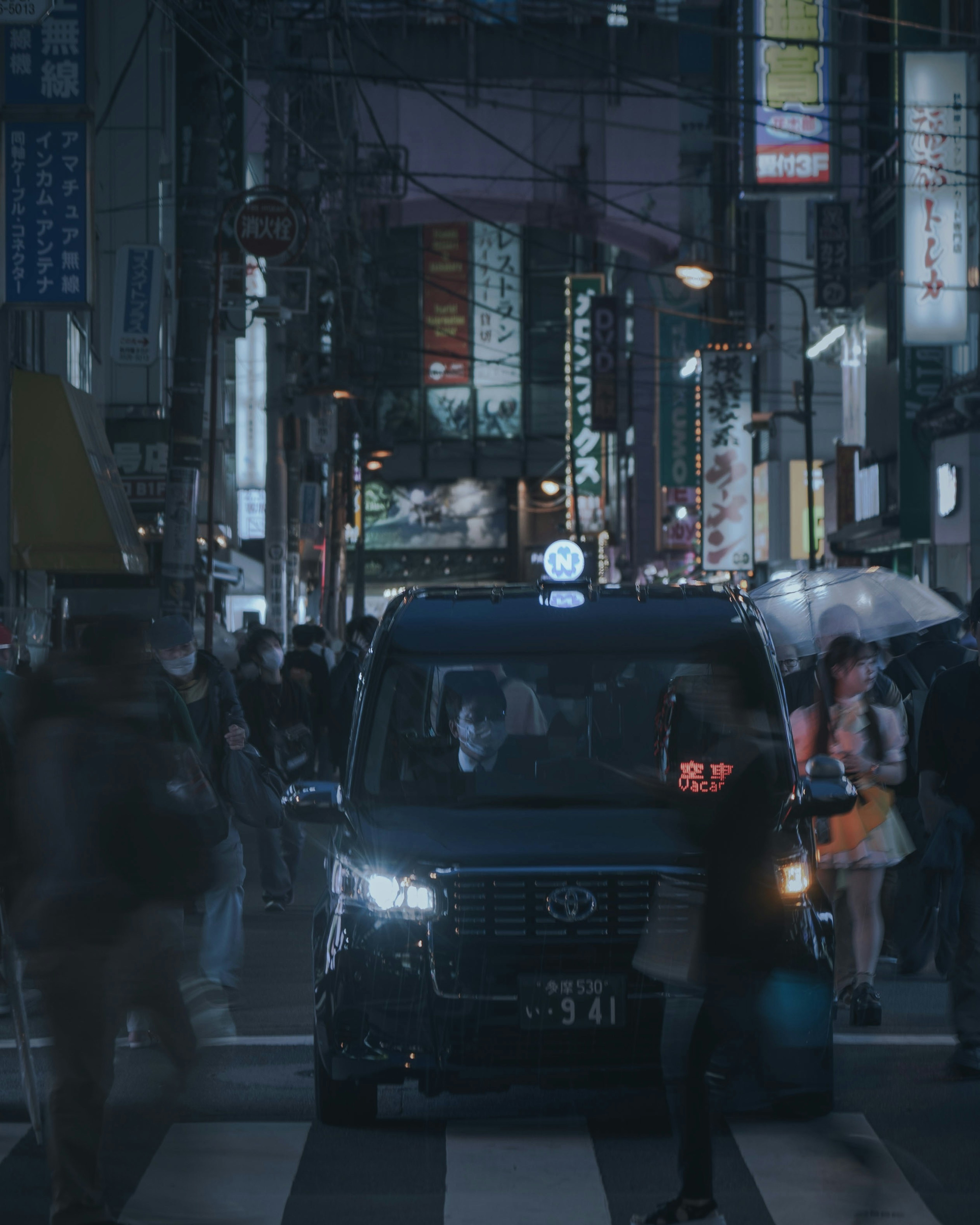 Taxi at a city intersection with pedestrians holding umbrellas at night