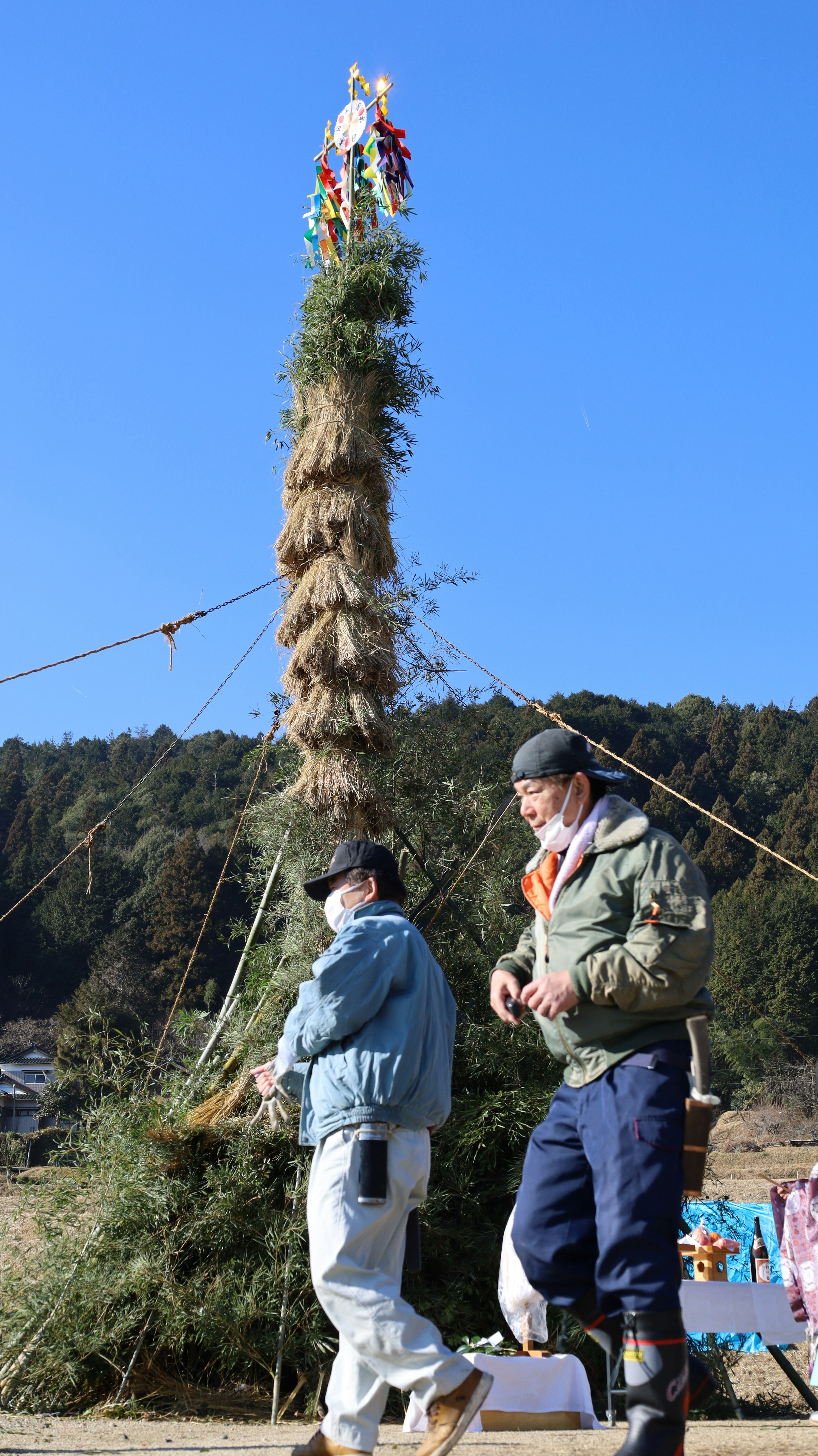 Two men standing near a tall straw tower in a rural setting