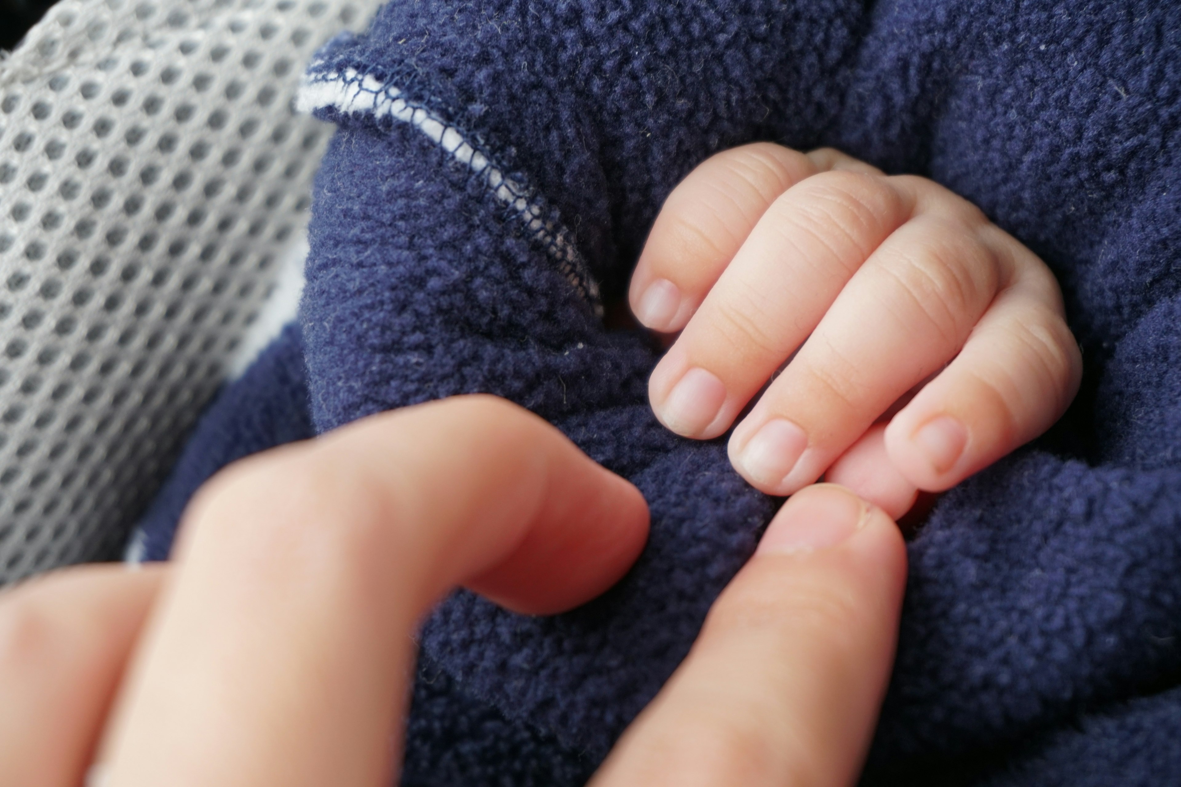 La pequeña mano de un bebé tocando otra mano envuelta en una manta azul