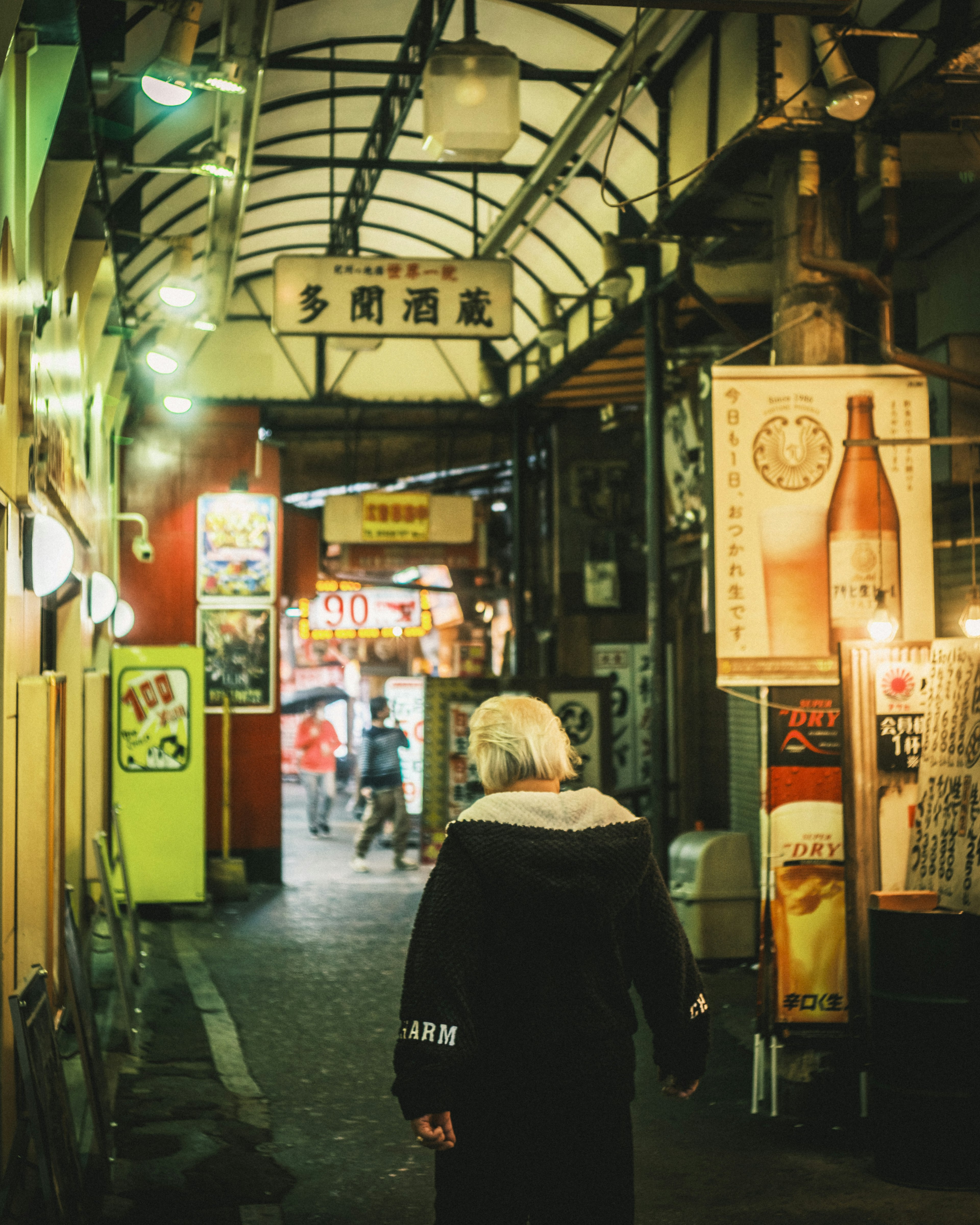 Elderly person walking down a narrow alley with bright signs and a covered walkway