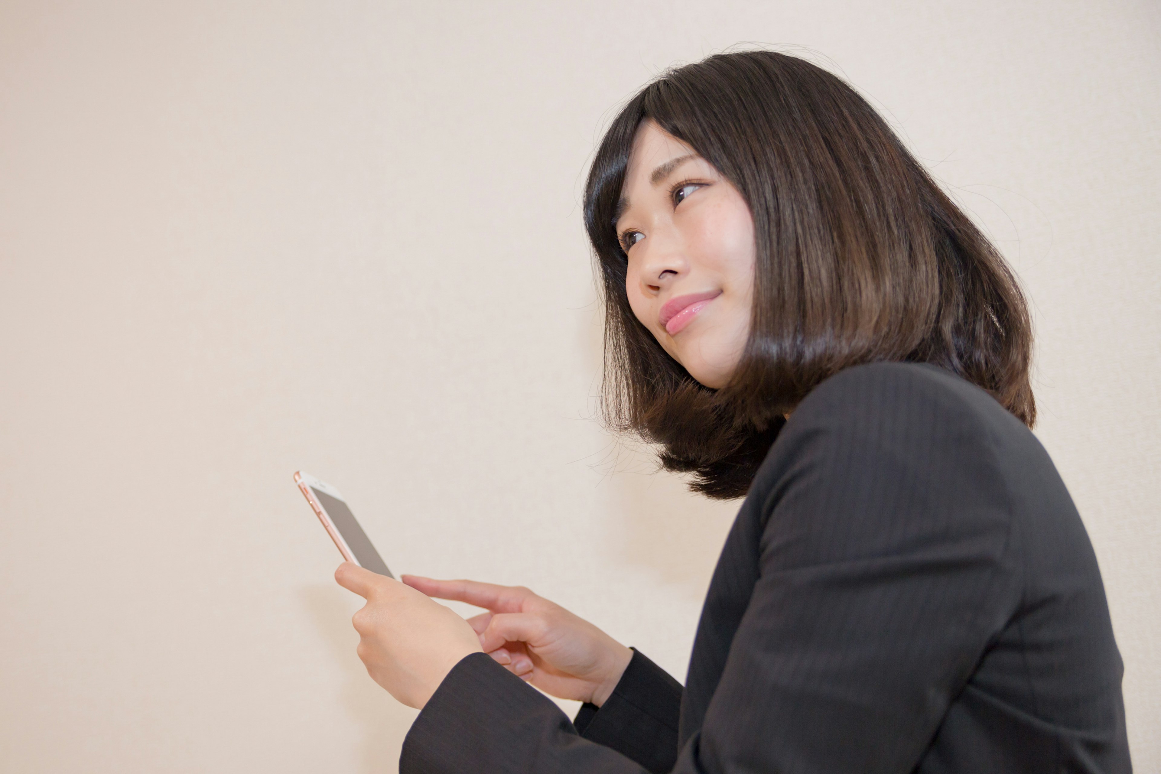 Una donna in abito da lavoro tiene uno smartphone e guarda pensierosa sorridendo