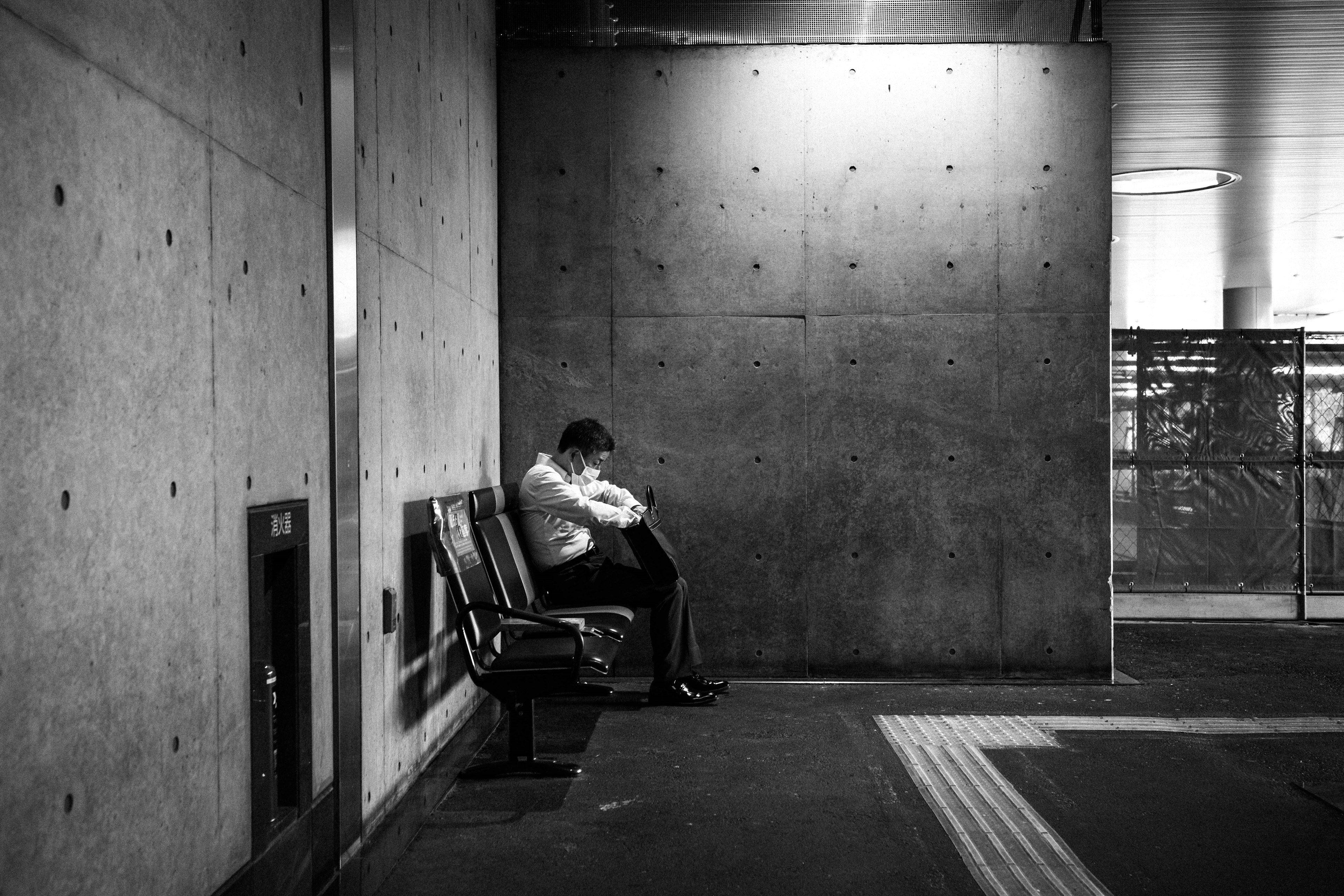 Black and white photo of a man sitting in front of a concrete wall