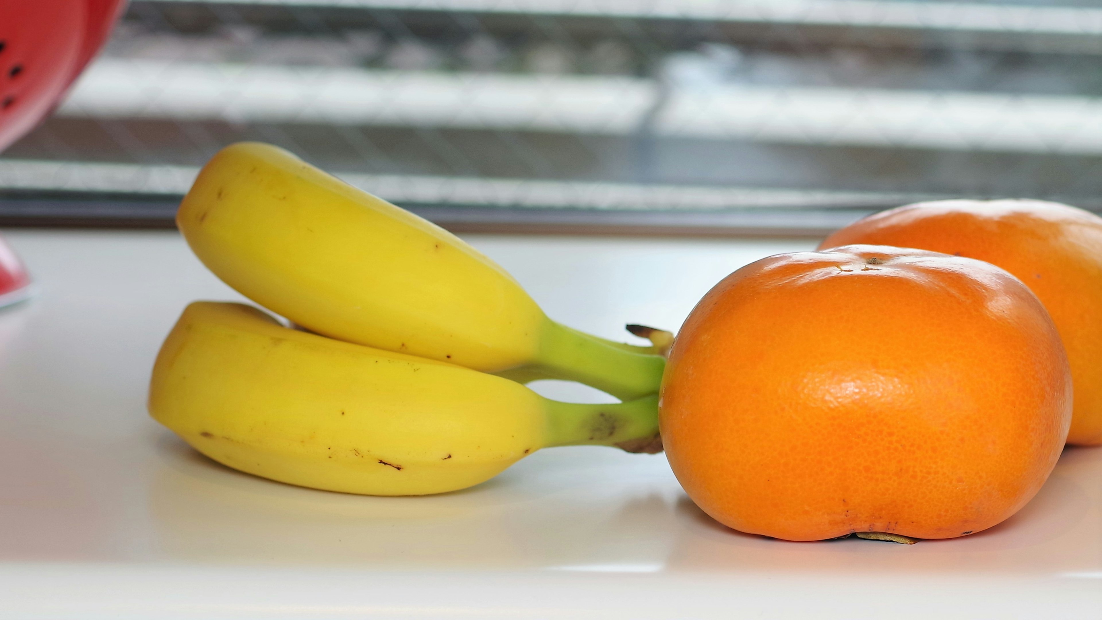 Gelbe Bananen und ein orangefarbener Kaki auf einem Küchentisch