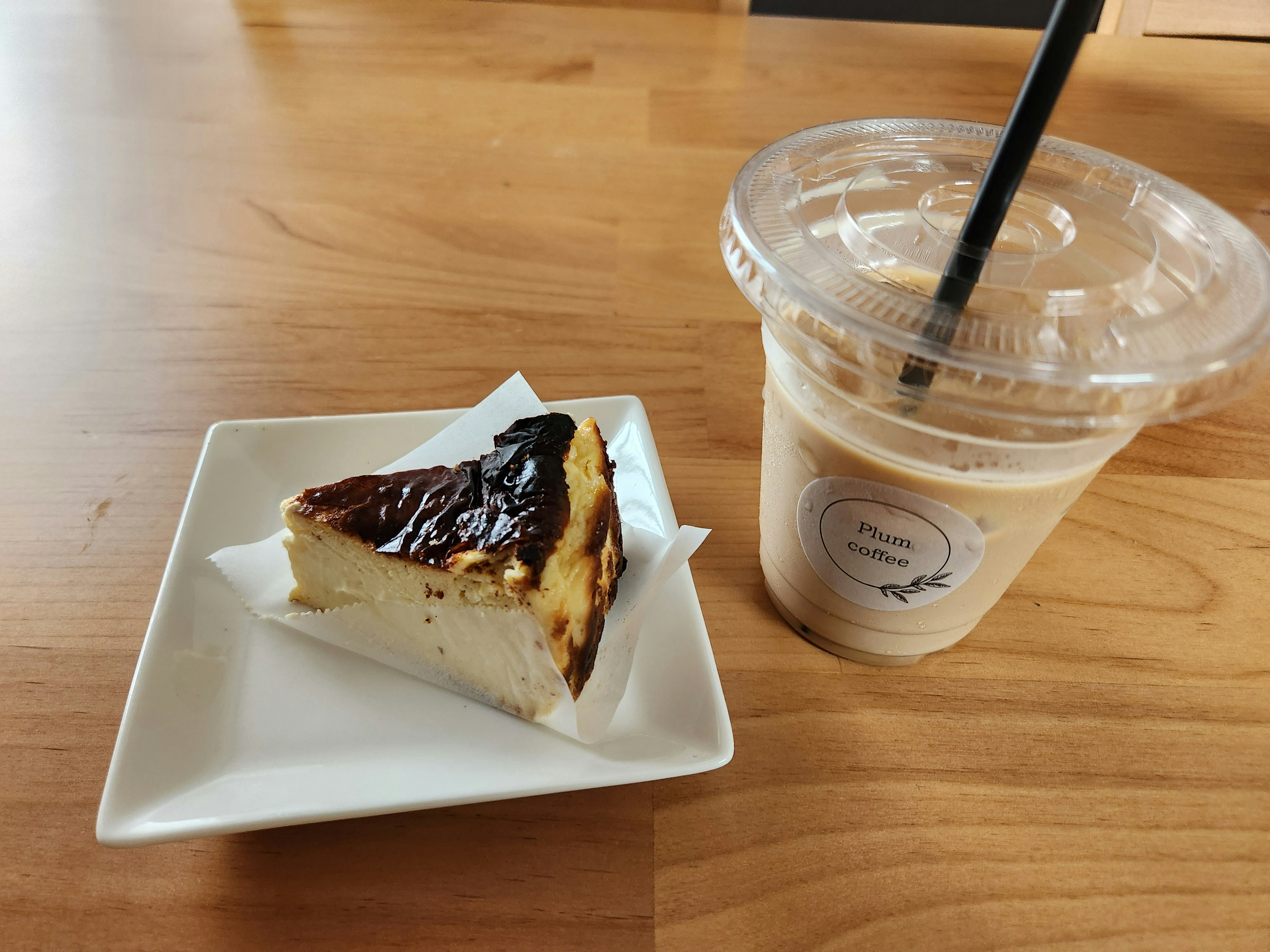 Una rebanada de tarta de queso en un plato blanco junto a un café helado en un vaso transparente