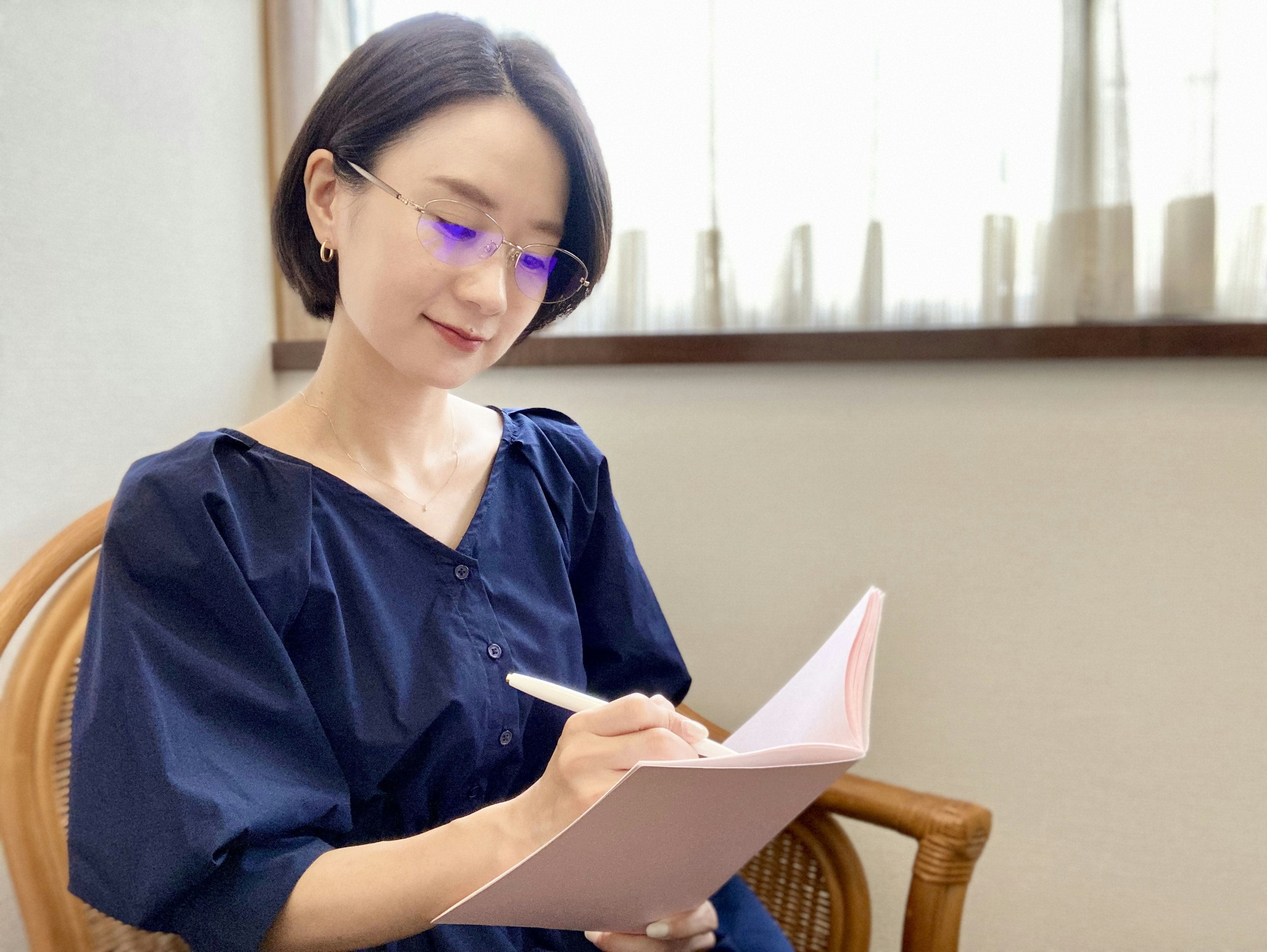 Woman wearing blue glasses writing in a pink notebook