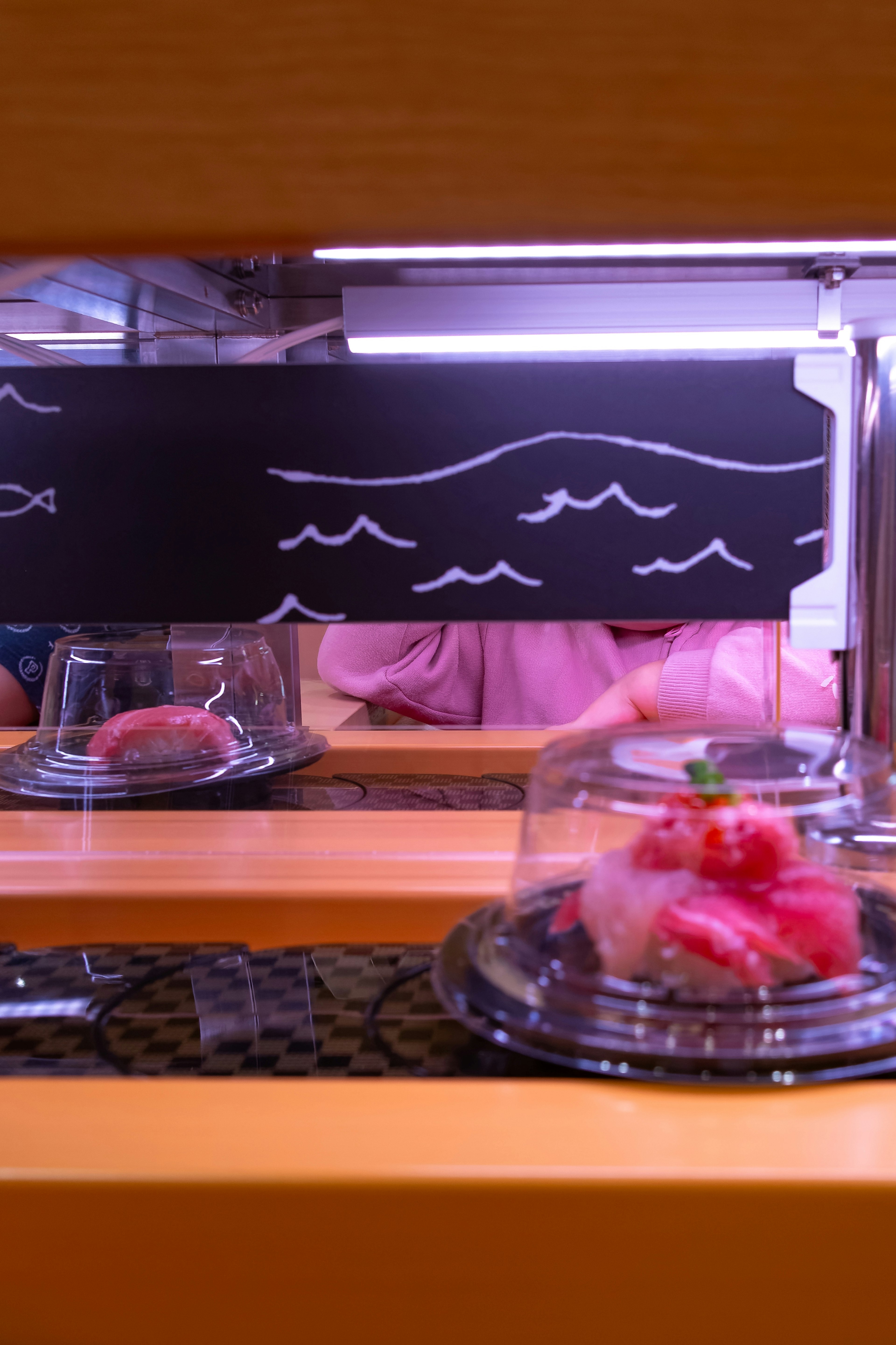 Sushi exposé sur un comptoir avec un tableau noir présentant des dessins de vagues