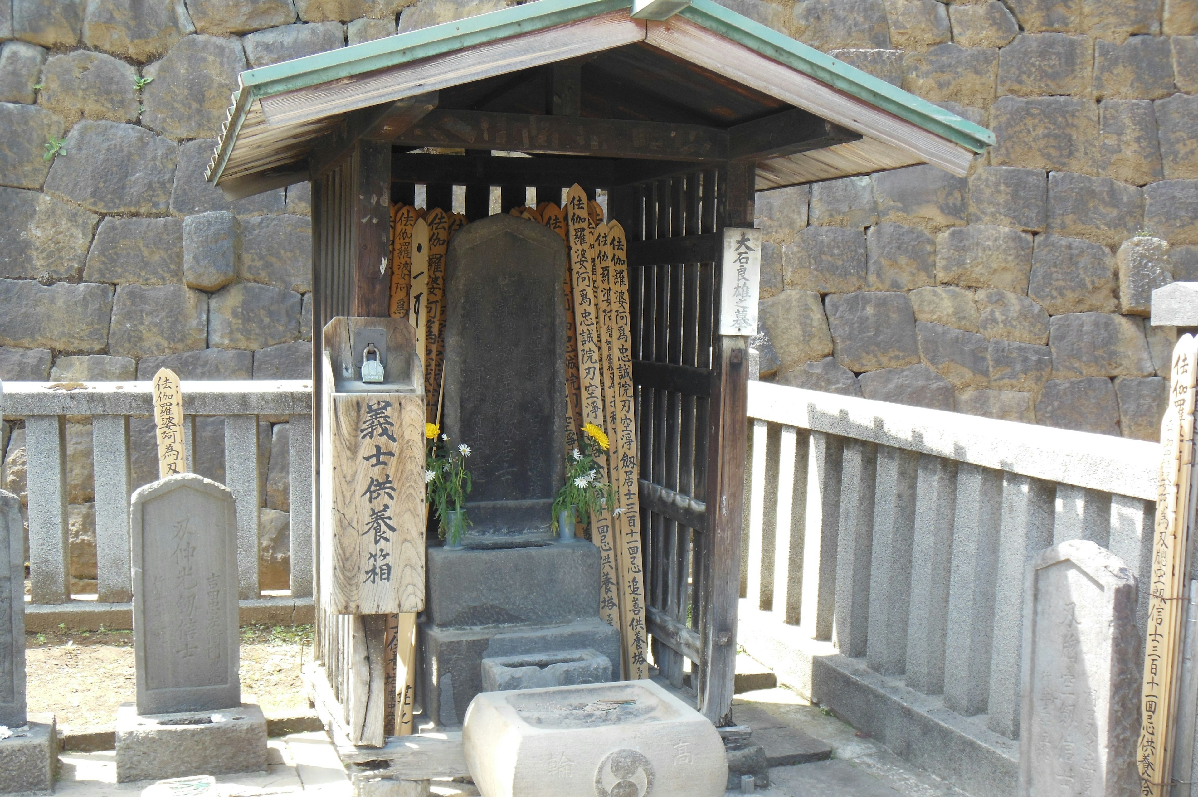 Une petite cabane contenant une statue en pierre avec des fleurs devant