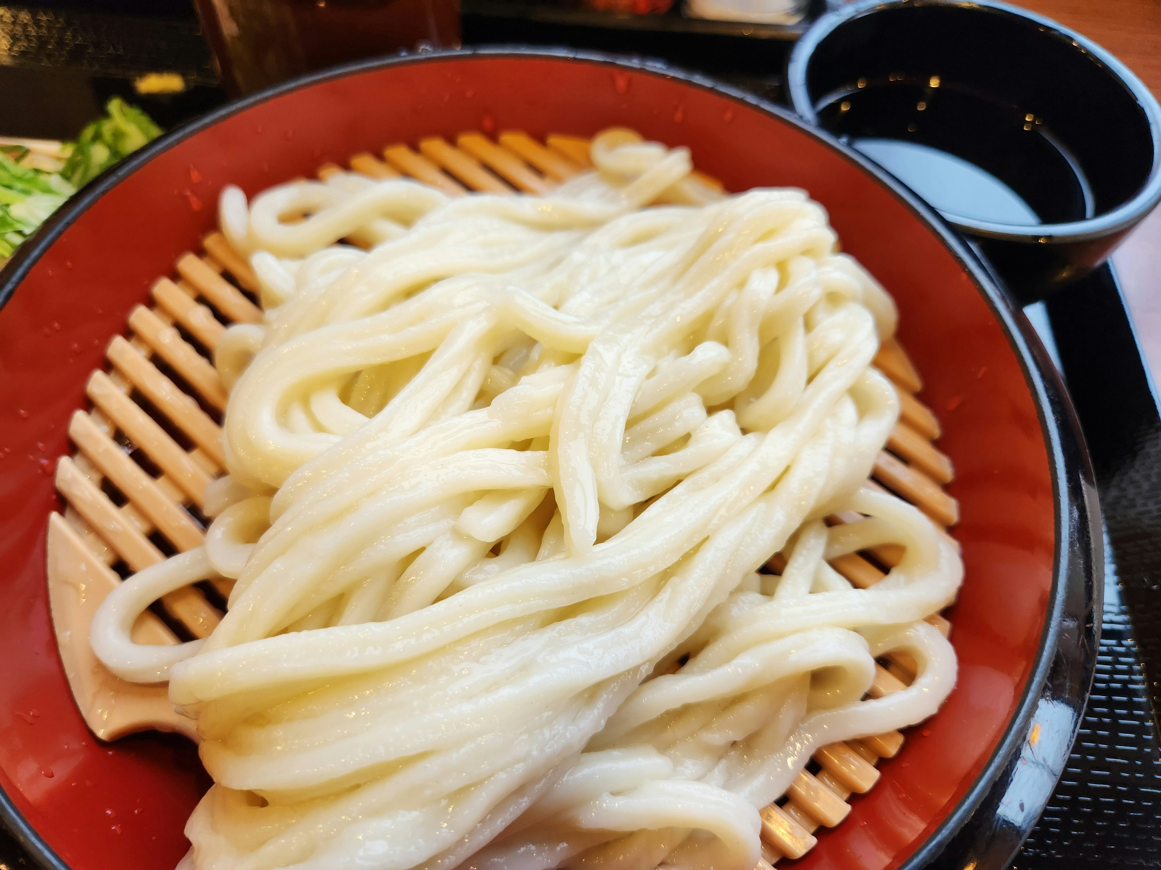 Udon zaru presentado en un tazón rojo con un pequeño plato negro al lado