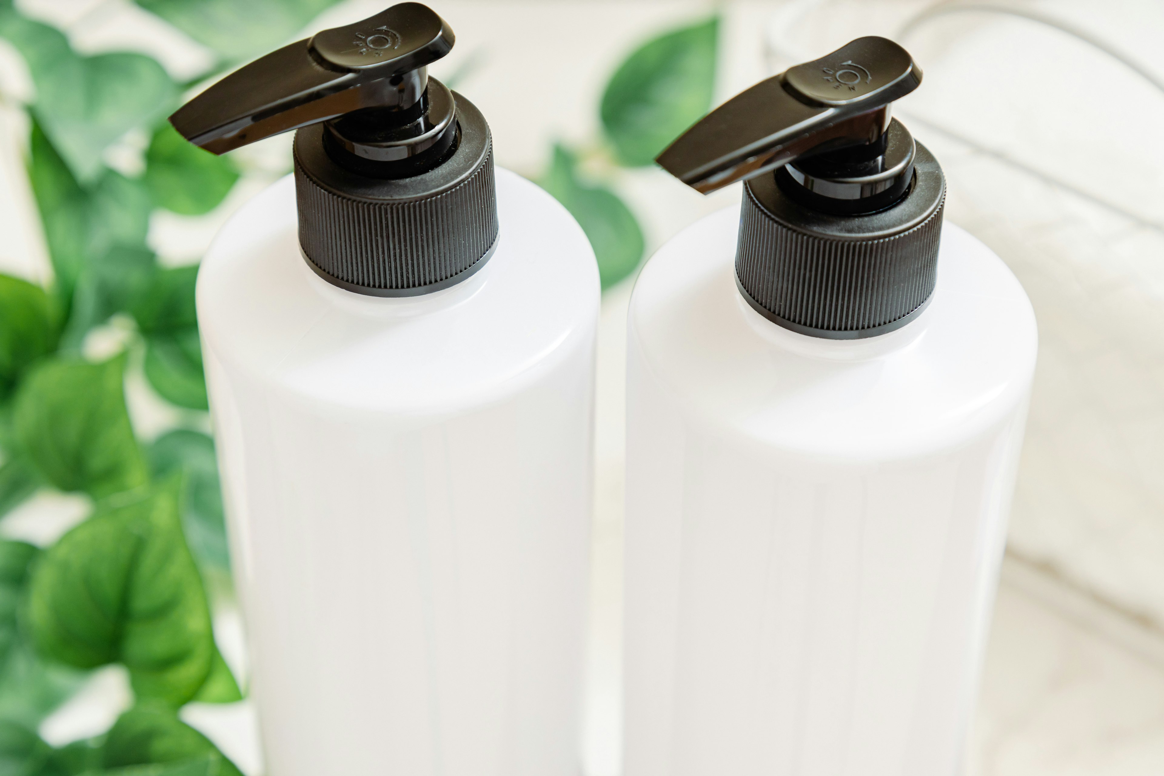 Two white bottles with black pump dispensers on a green leaf background