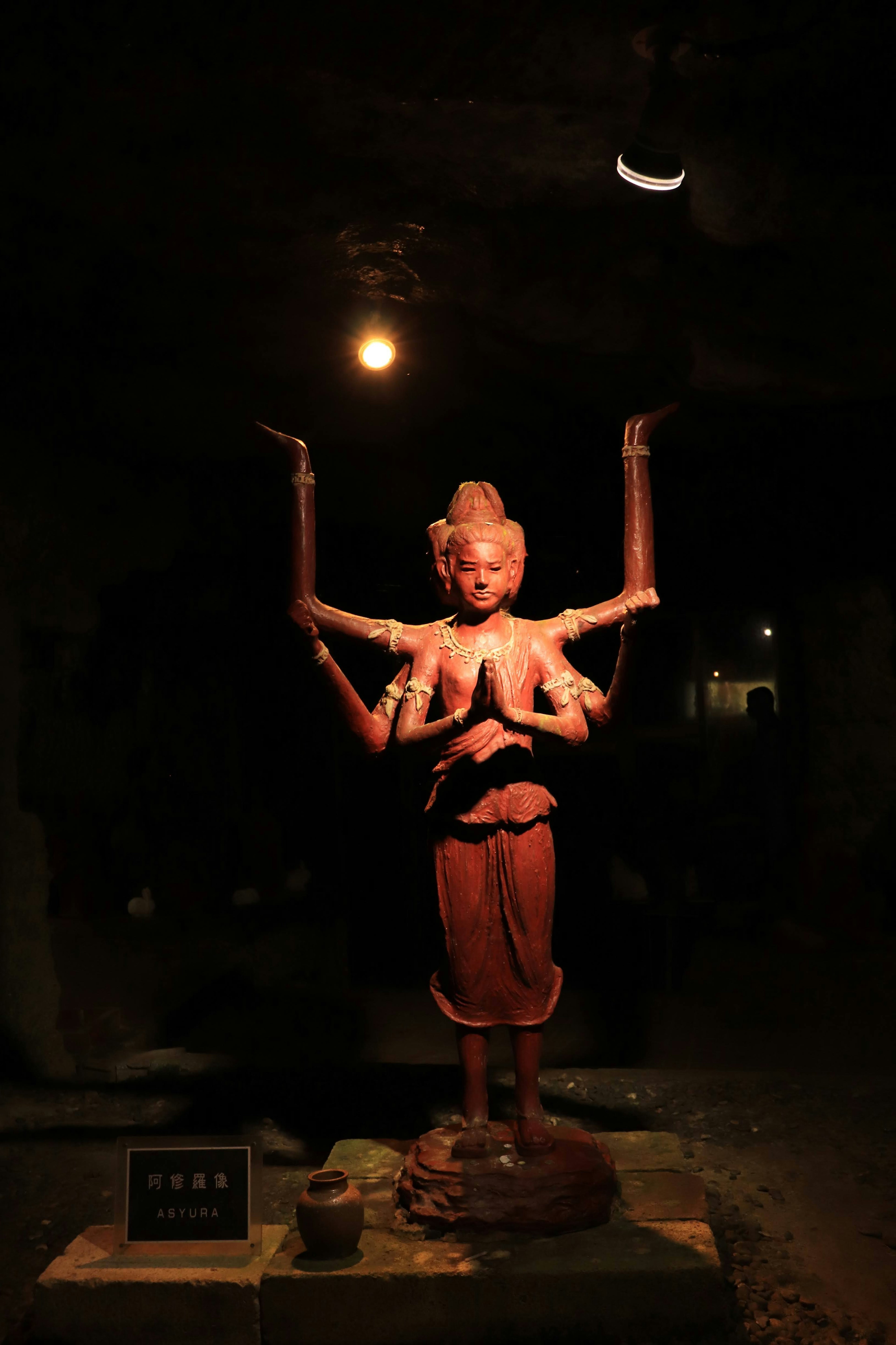 A multi-armed sculpture illuminated by a spotlight in a dark background