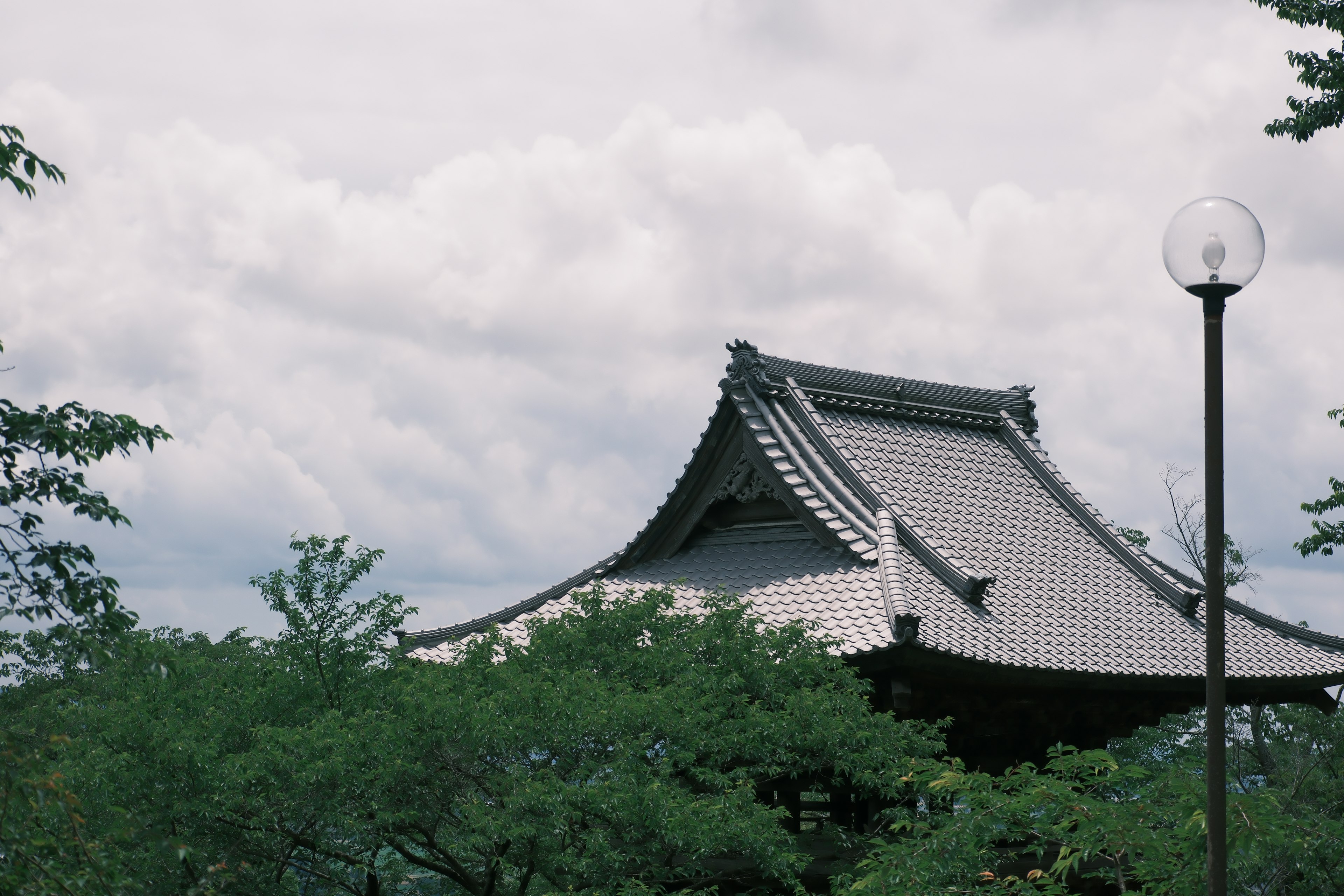 Traditionelles japanisches Tempeldach umgeben von Grün und einer Straßenlaterne