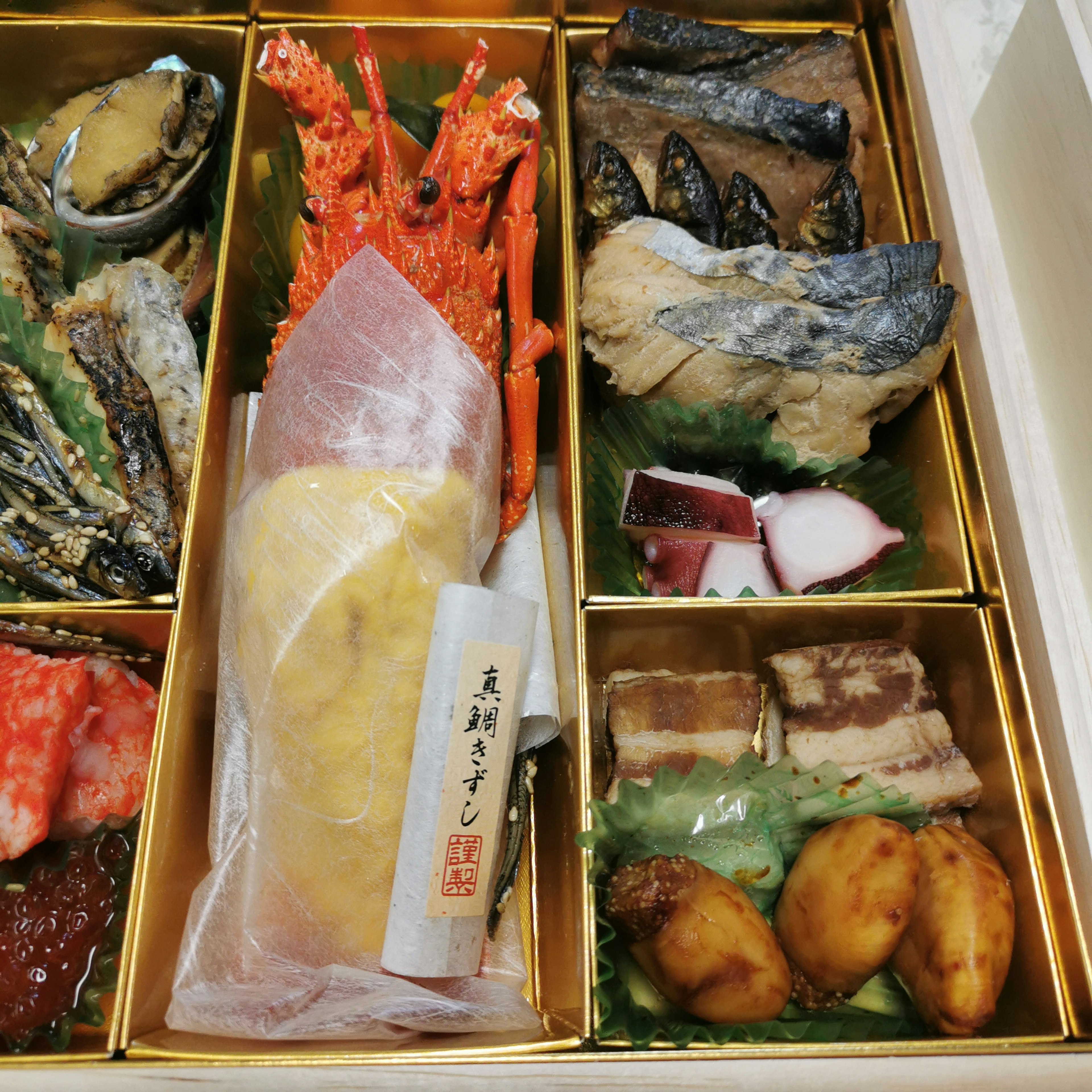 A luxurious assortment of Japanese cuisine in a bento box featuring seafood and meat dishes beautifully arranged