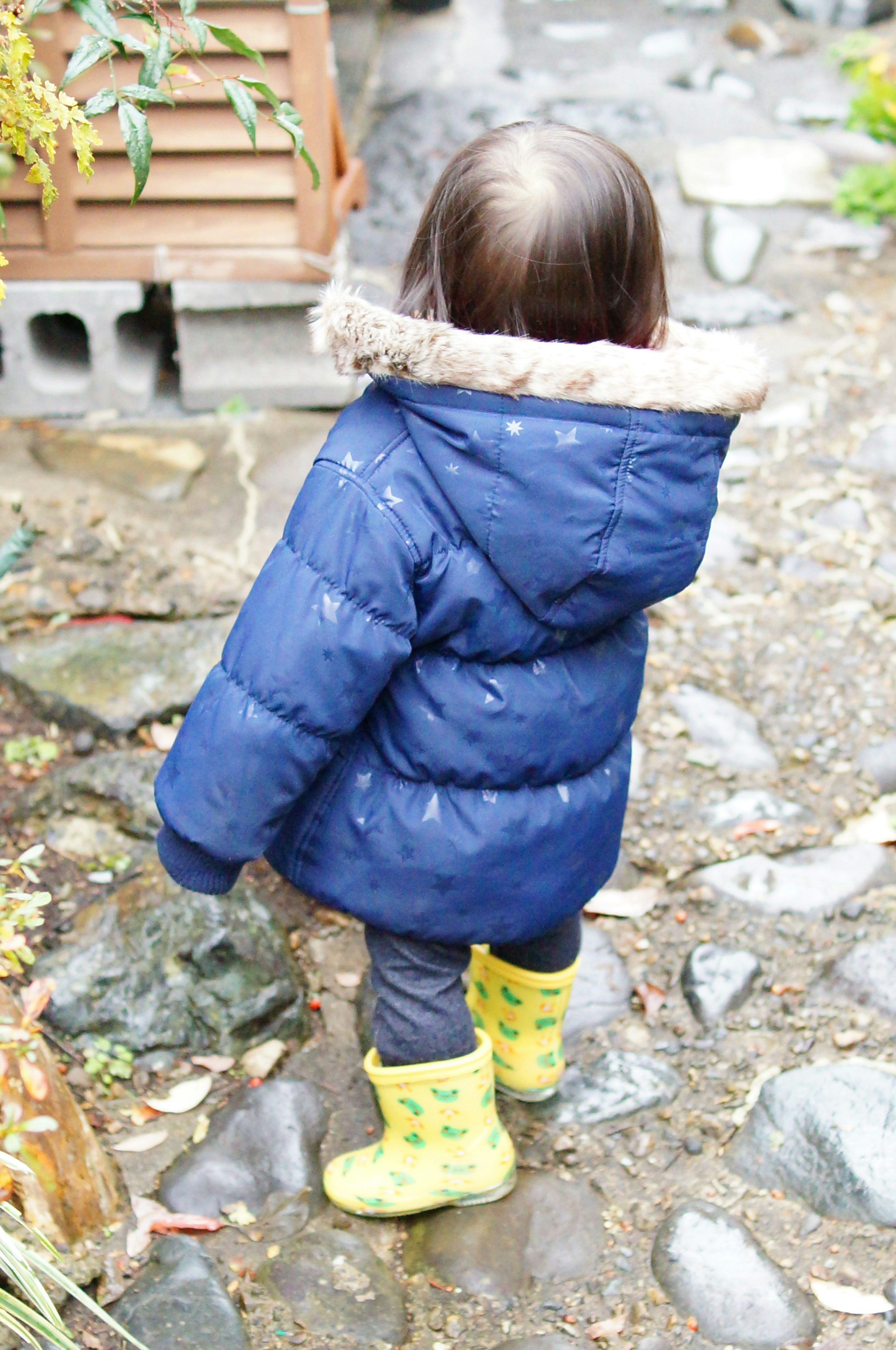 Child in a blue puffer jacket standing with back turned