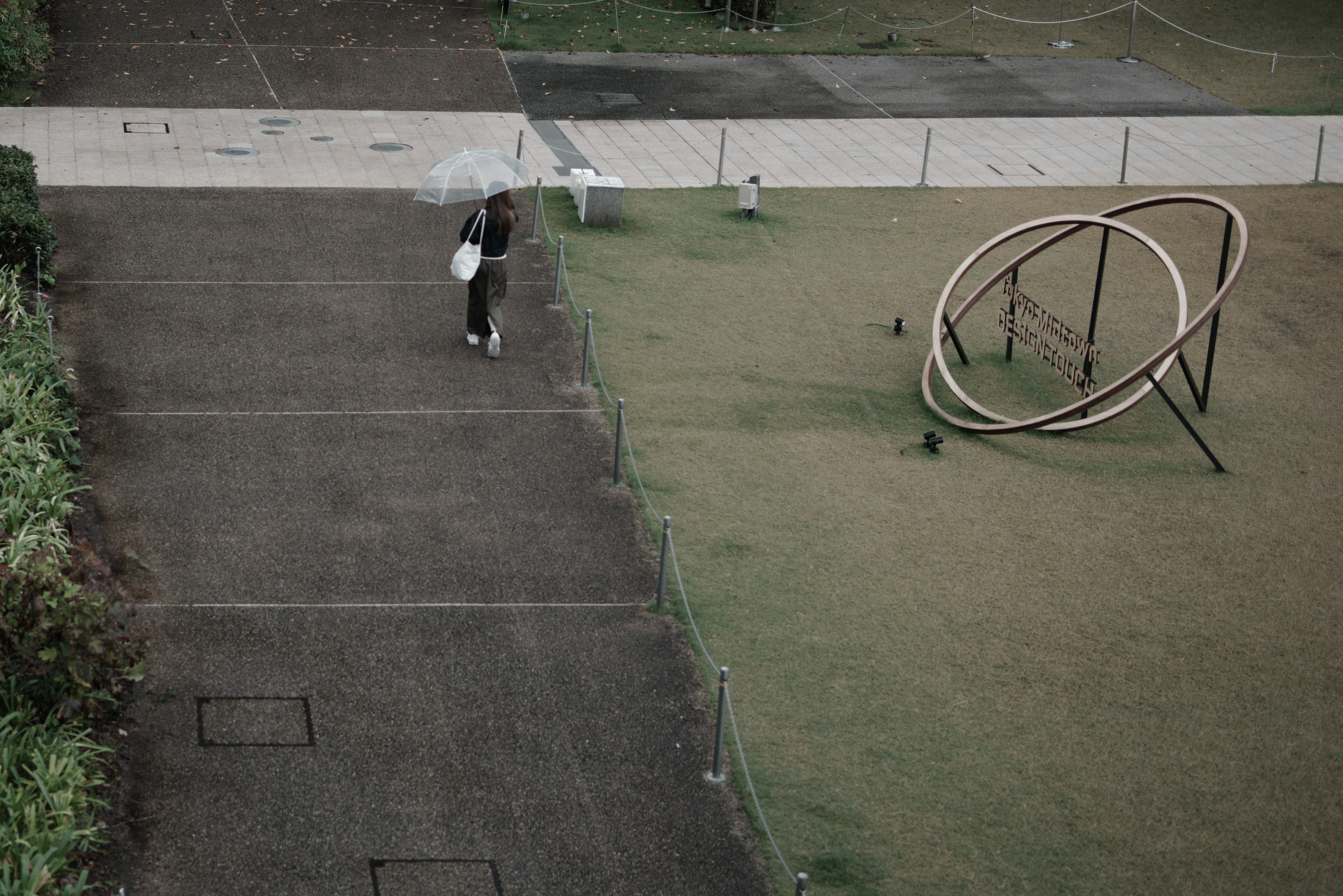 A person walking with an umbrella near playground equipment in a park