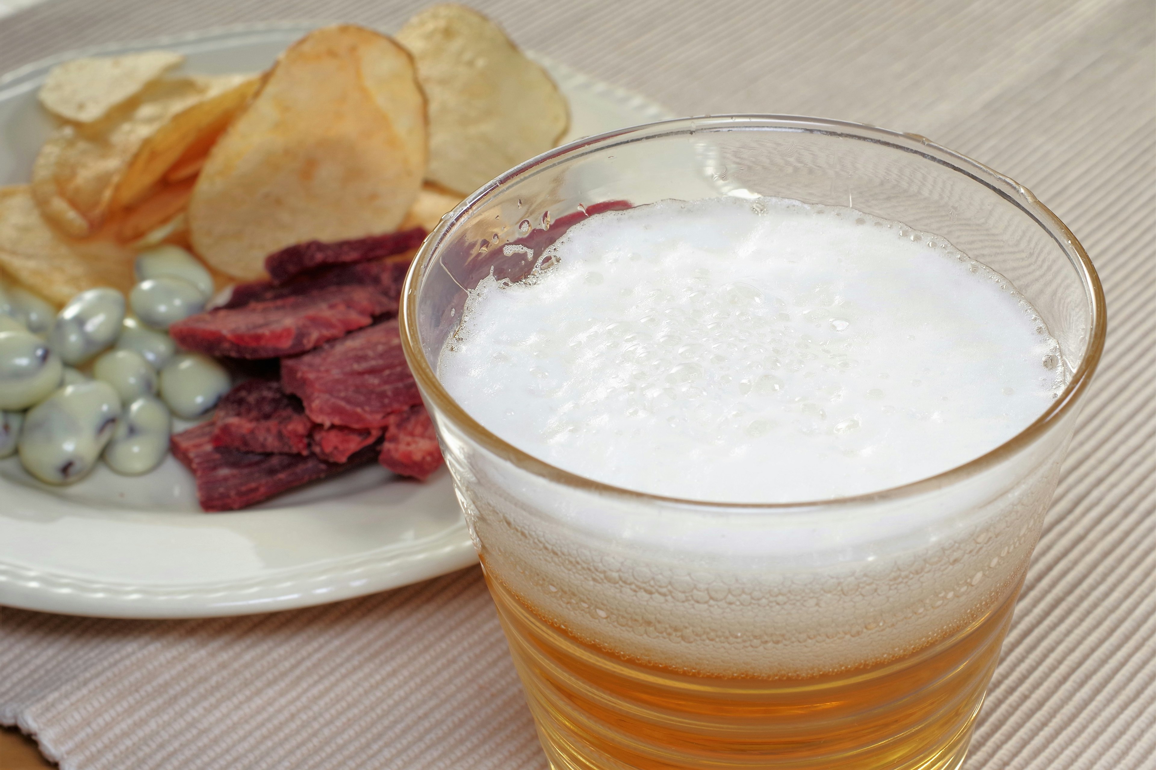 Image of a glass of beer with a plate of snacks including chips and jerky