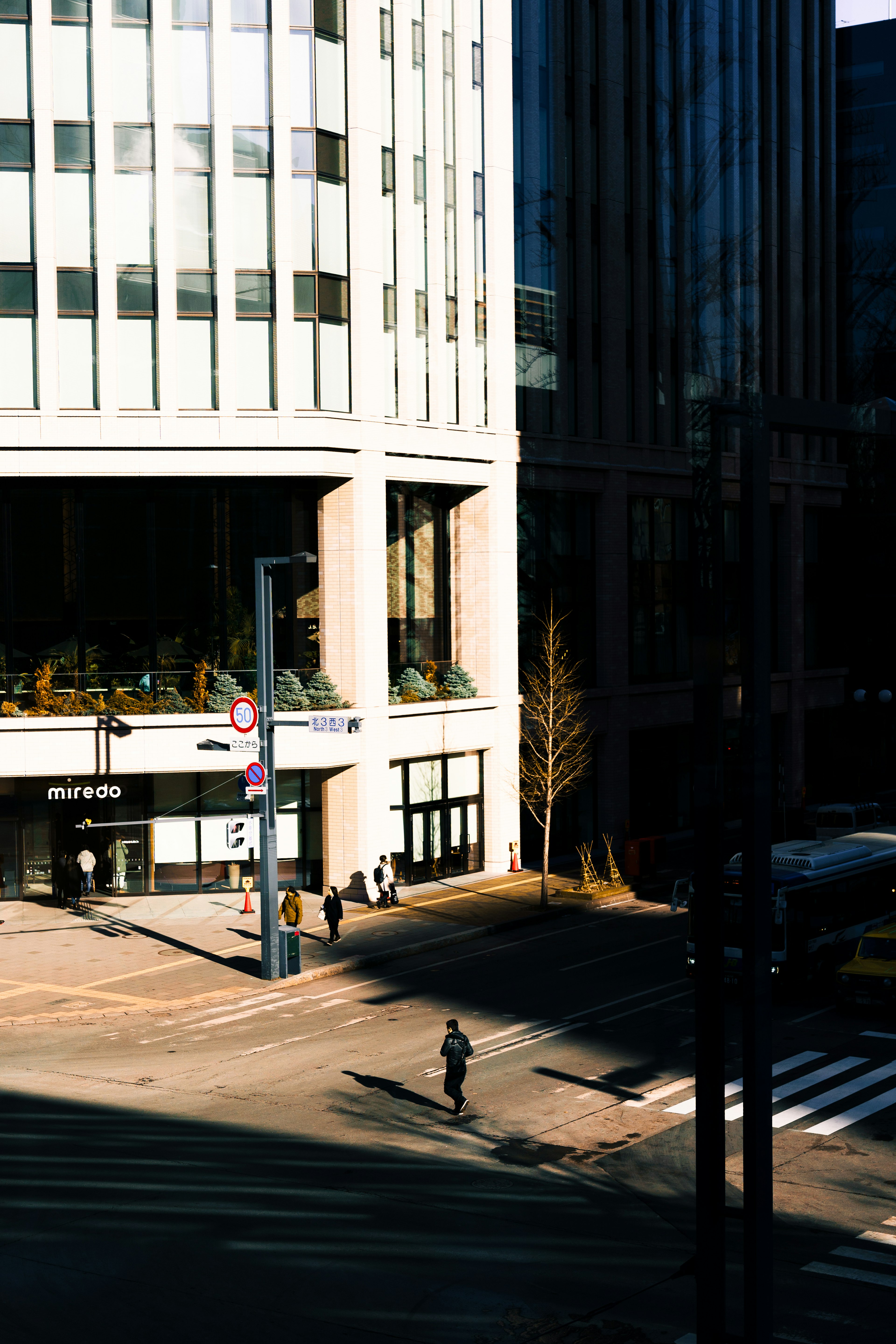 A man standing at a crosswalk with modern buildings in the background