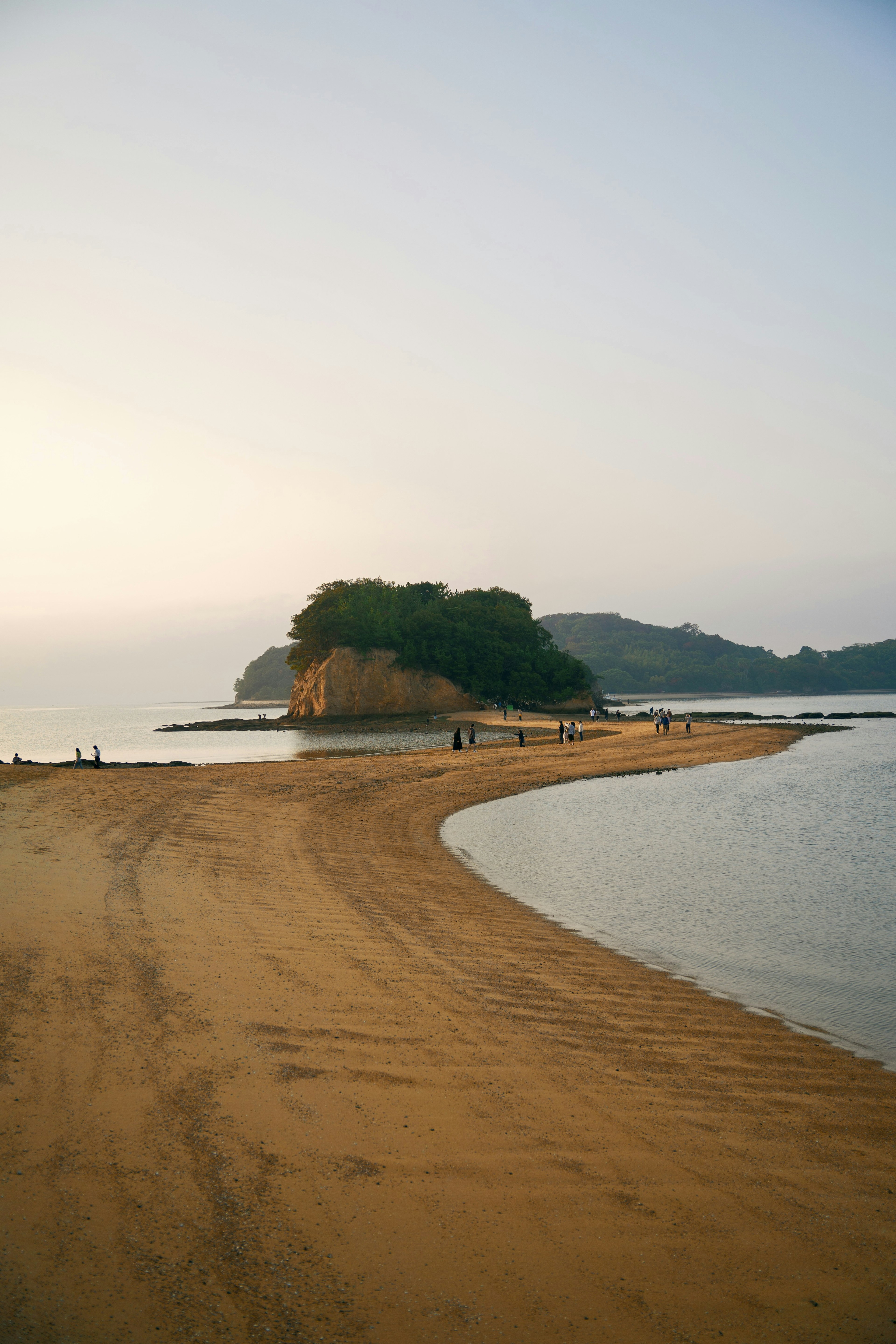 Vue pittoresque d'une plage de sable se courbant autour d'une petite île au coucher du soleil