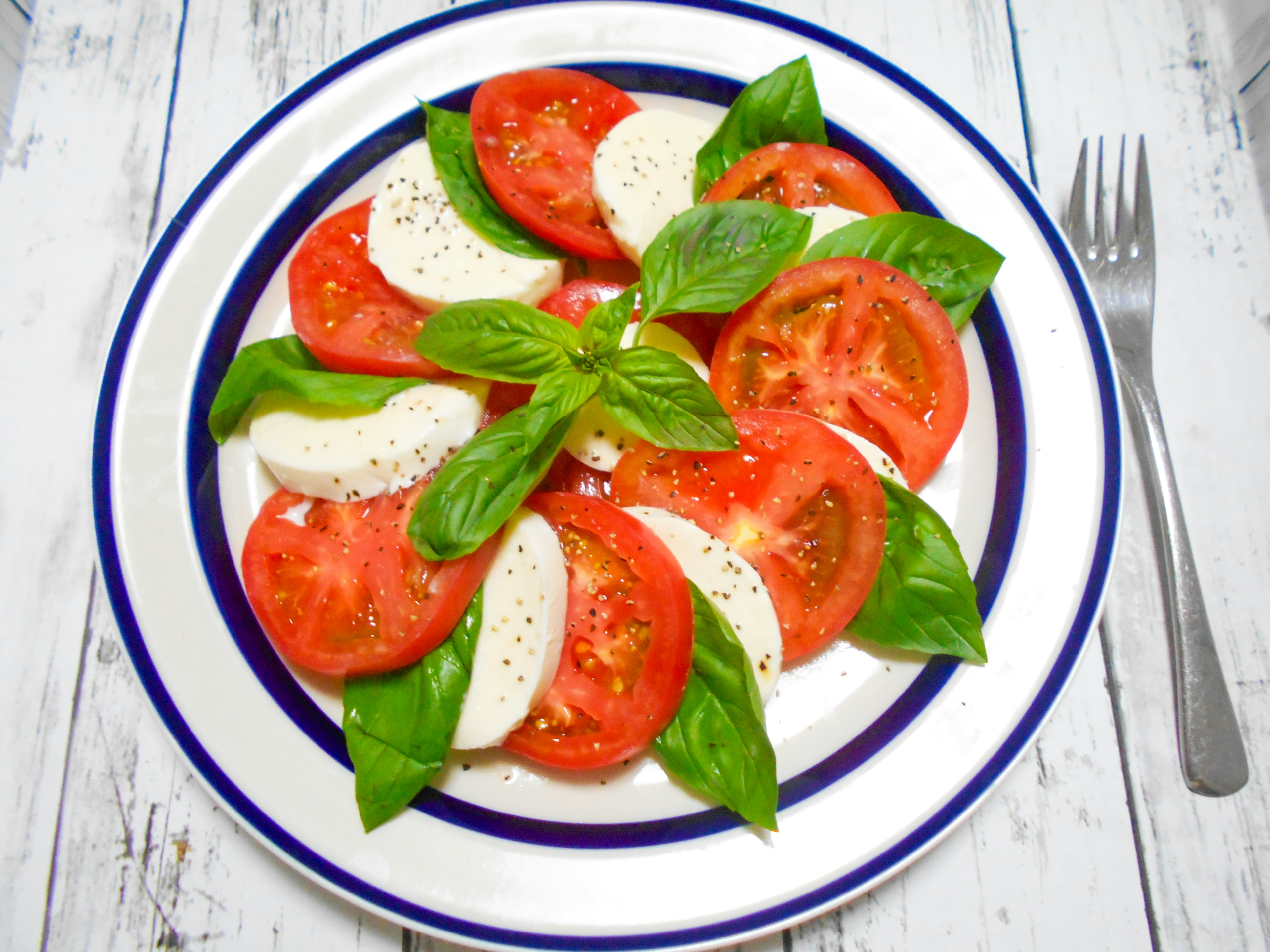 Teller mit Tomaten- und Mozzarella-Salat garniert mit Basilikum