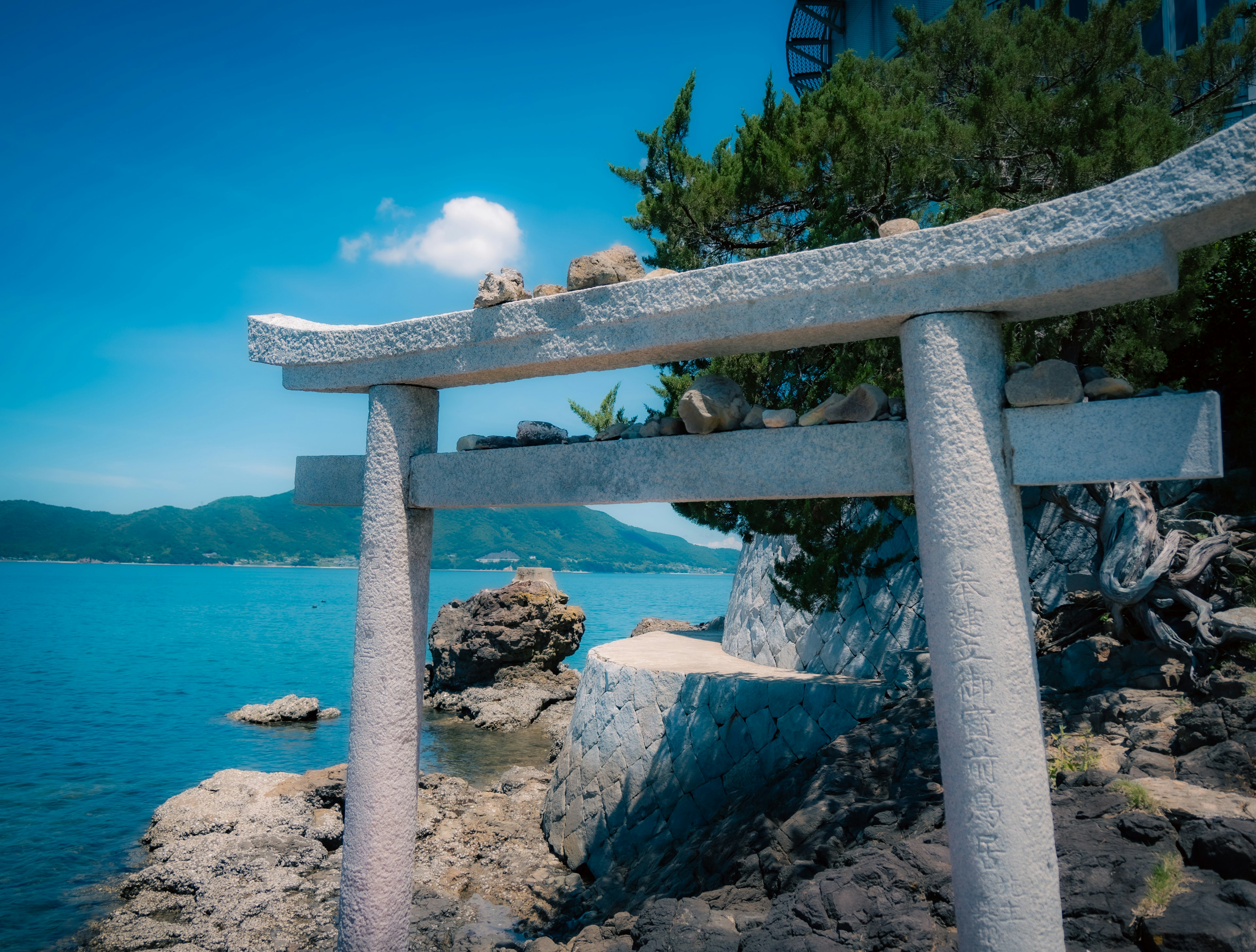 Puerta torii blanca junto al mar azul y cielo con costa rocosa