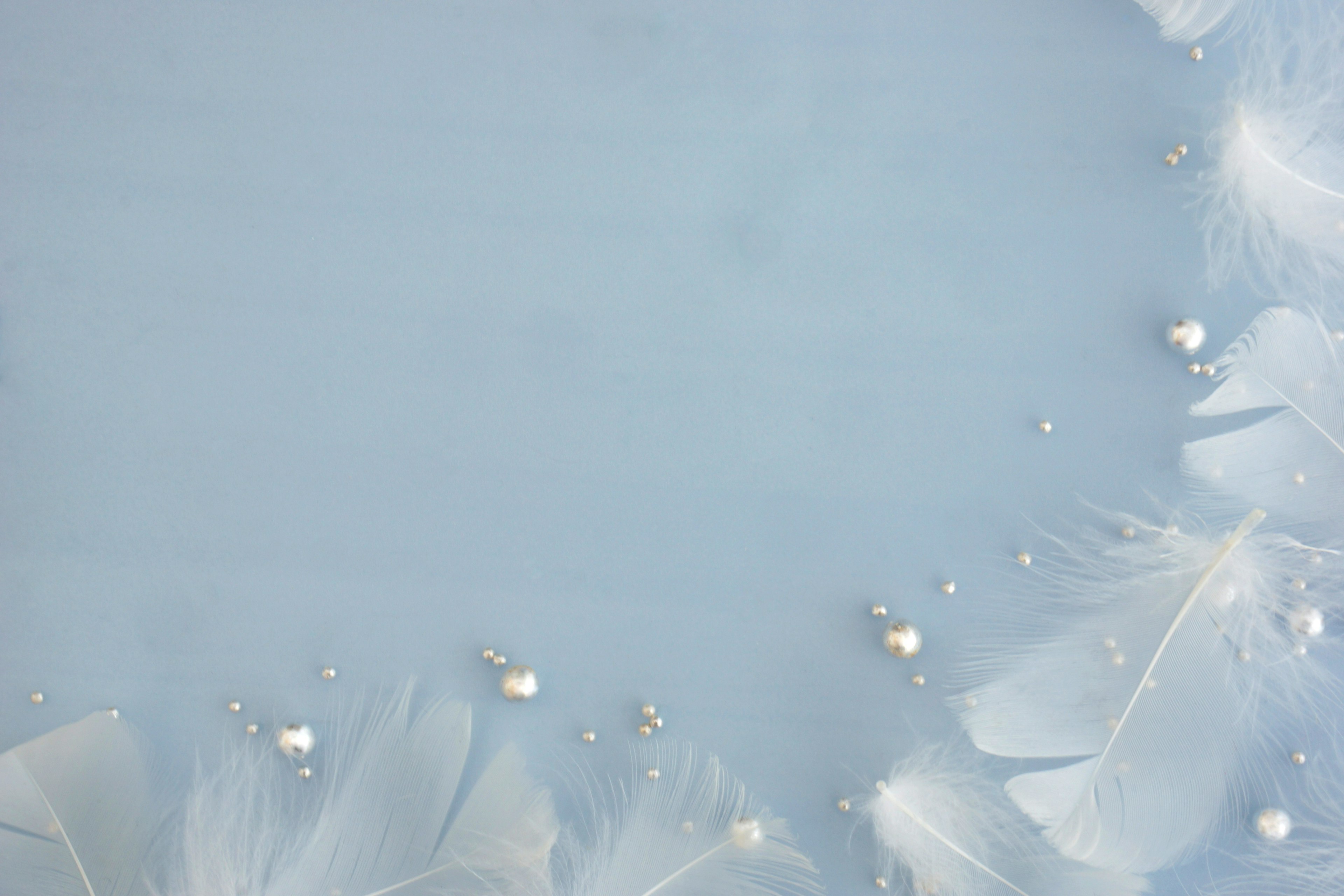 Soft blue background adorned with white feathers and shiny beads