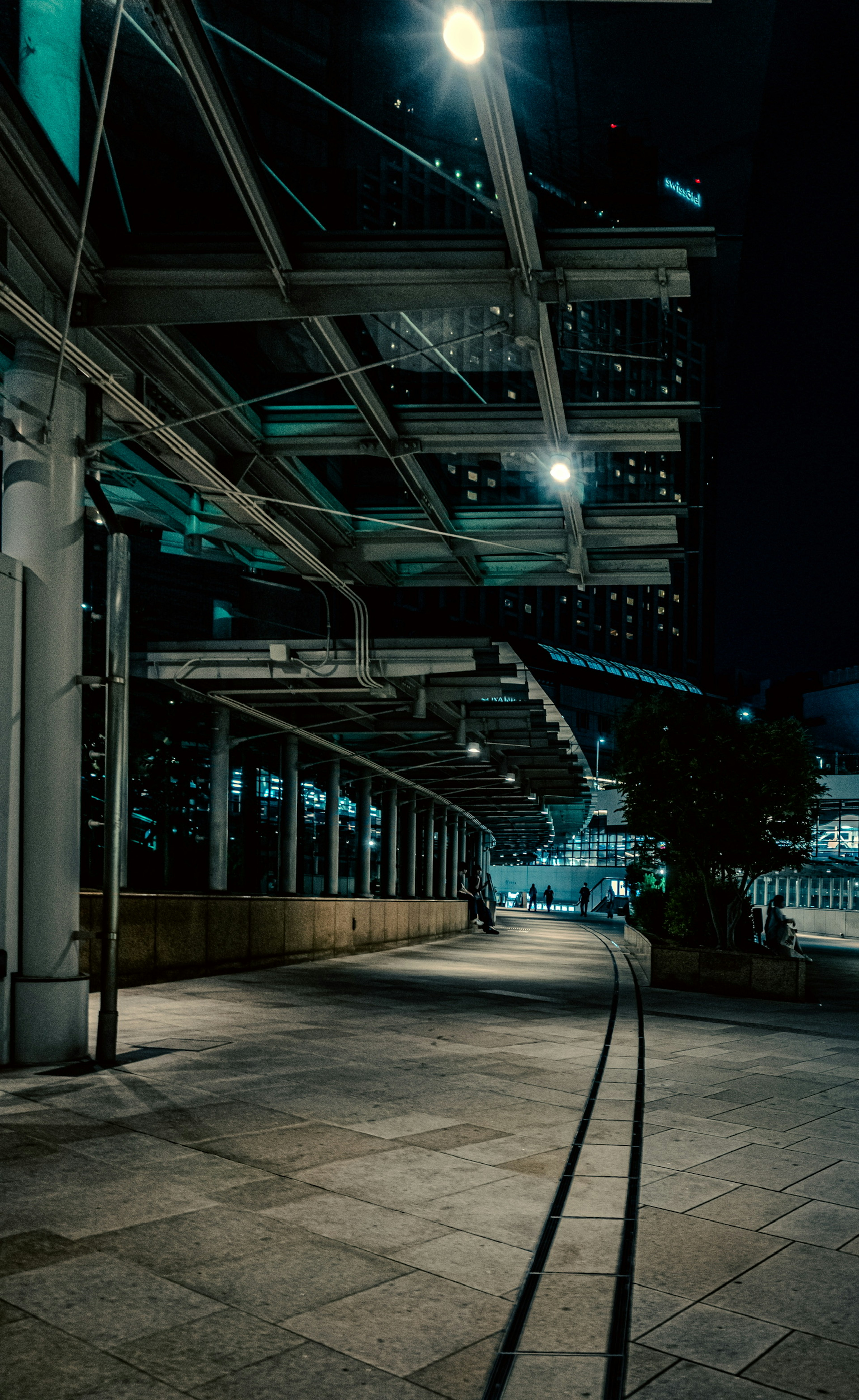 Nighttime urban walkway with bright streetlights and railway tracks