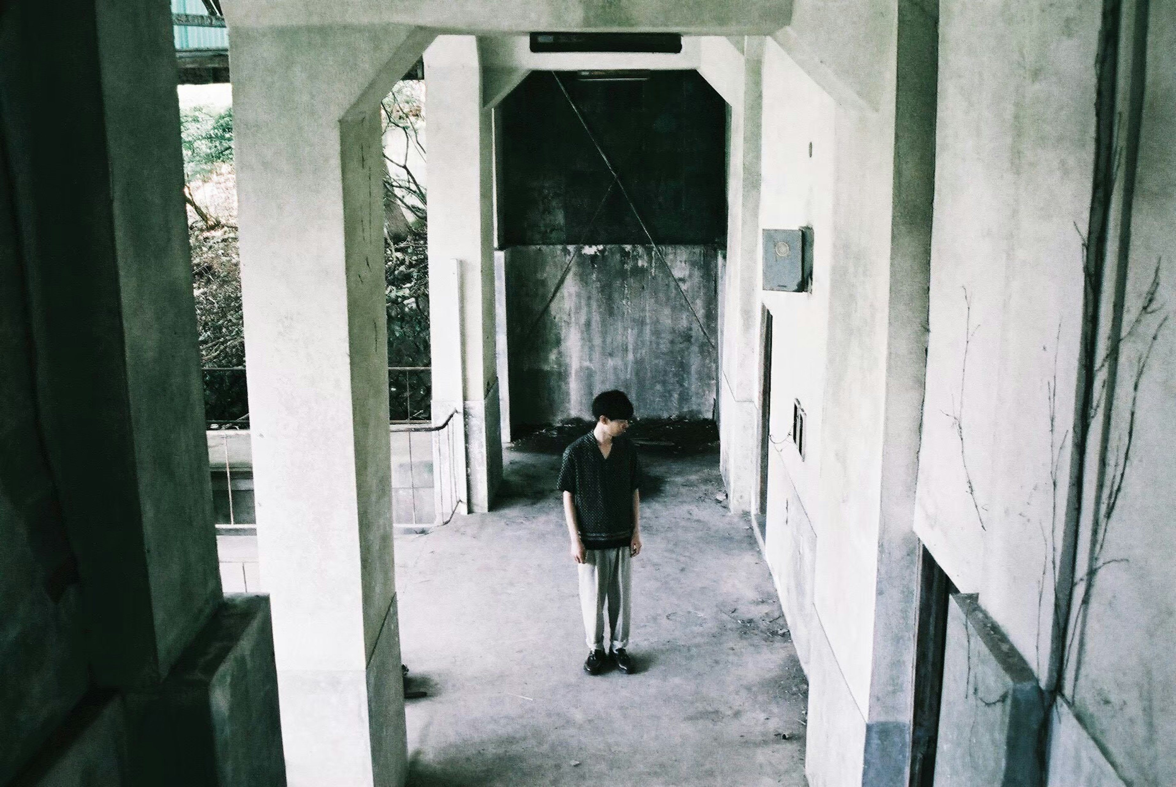 A boy standing in an empty corridor with concrete walls and floor