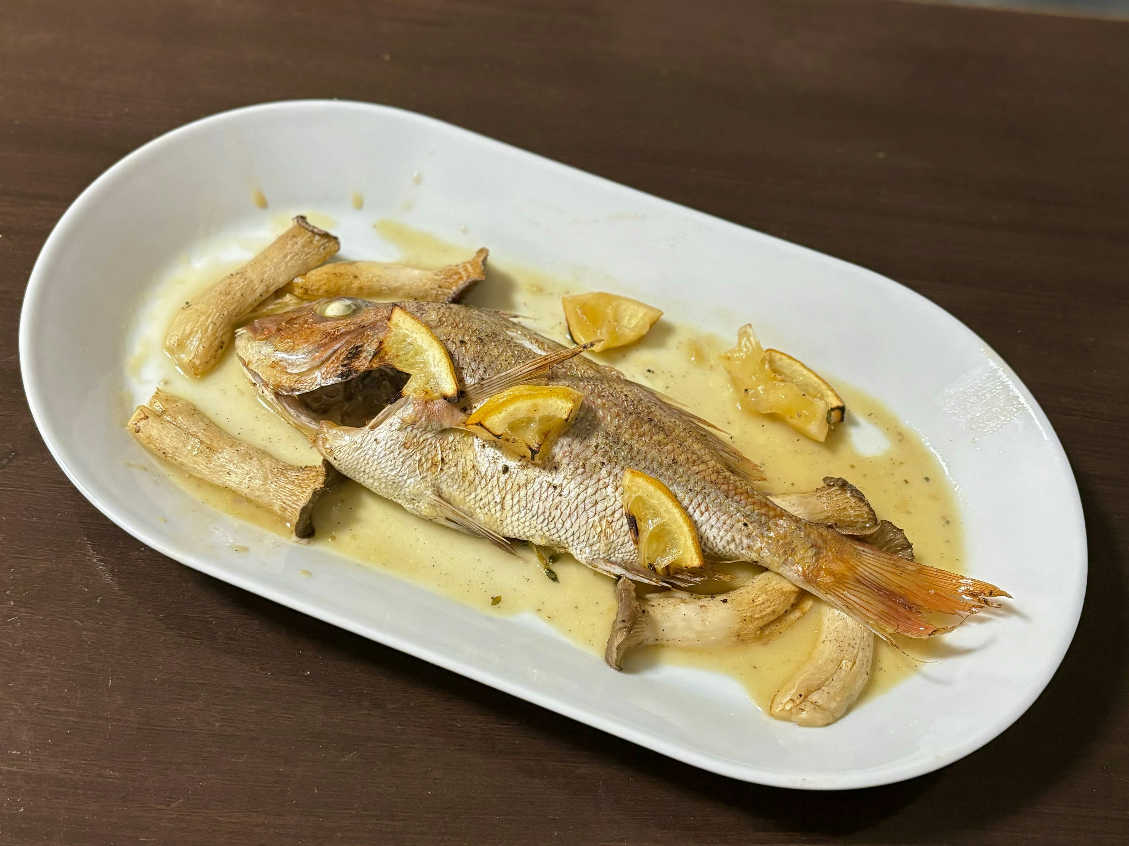 Baked fish served on a white plate with lemon and banana slices