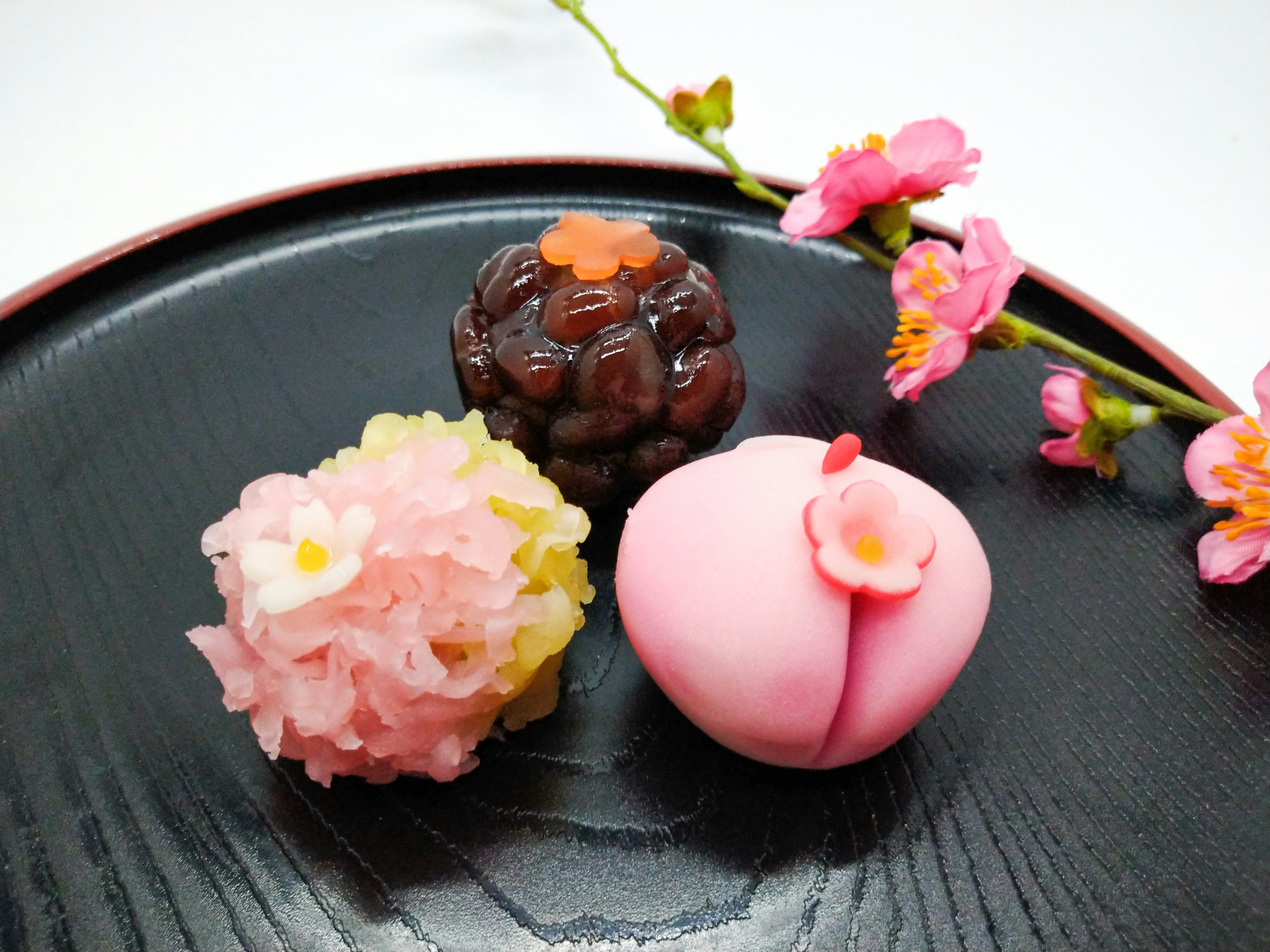 Kue Jepang yang indah disusun di atas piring hitam dengan dekorasi bunga sakura