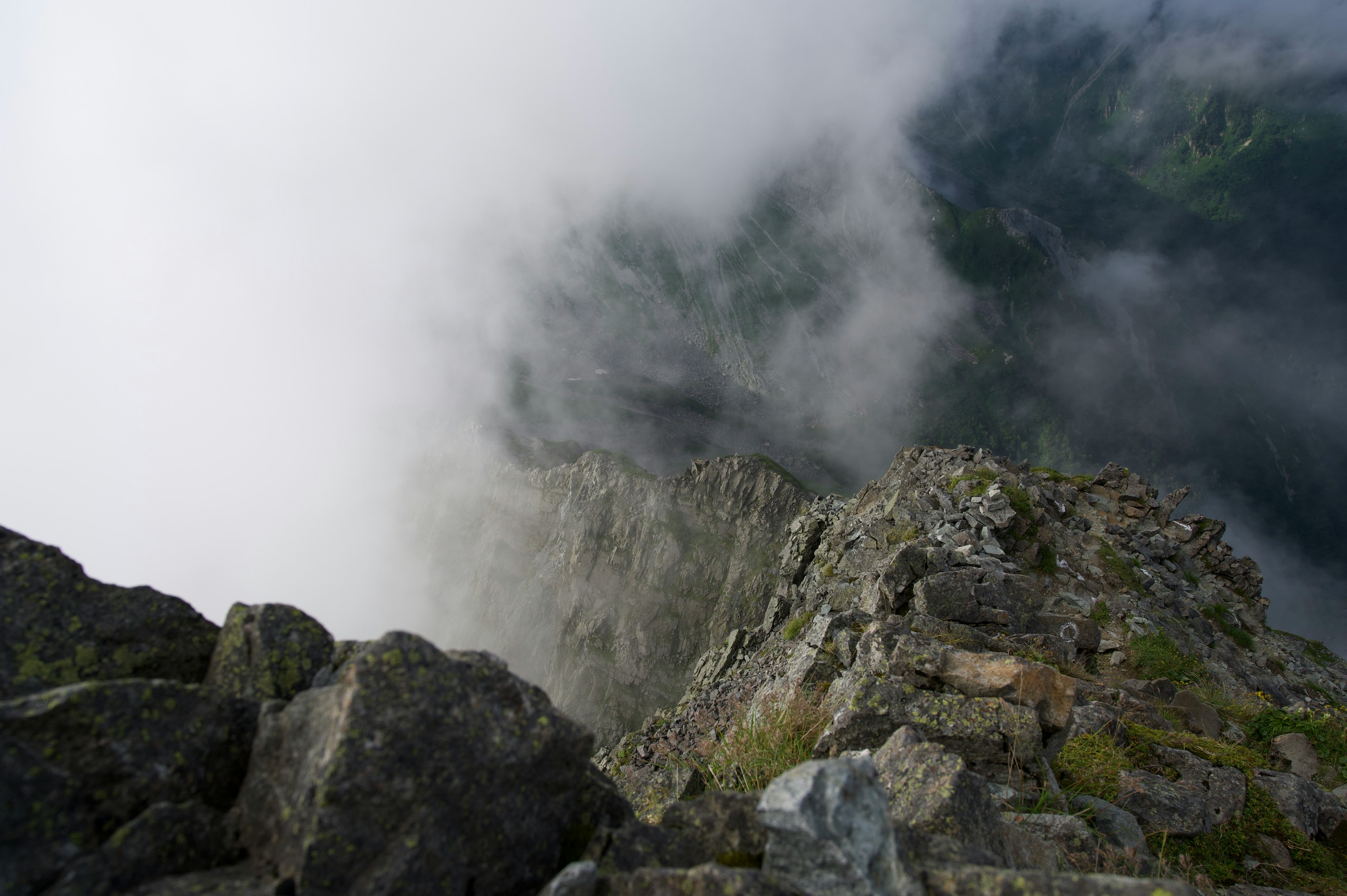 Vista dalla cima della montagna con nebbia che copre il paesaggio e affioramento roccioso visibile