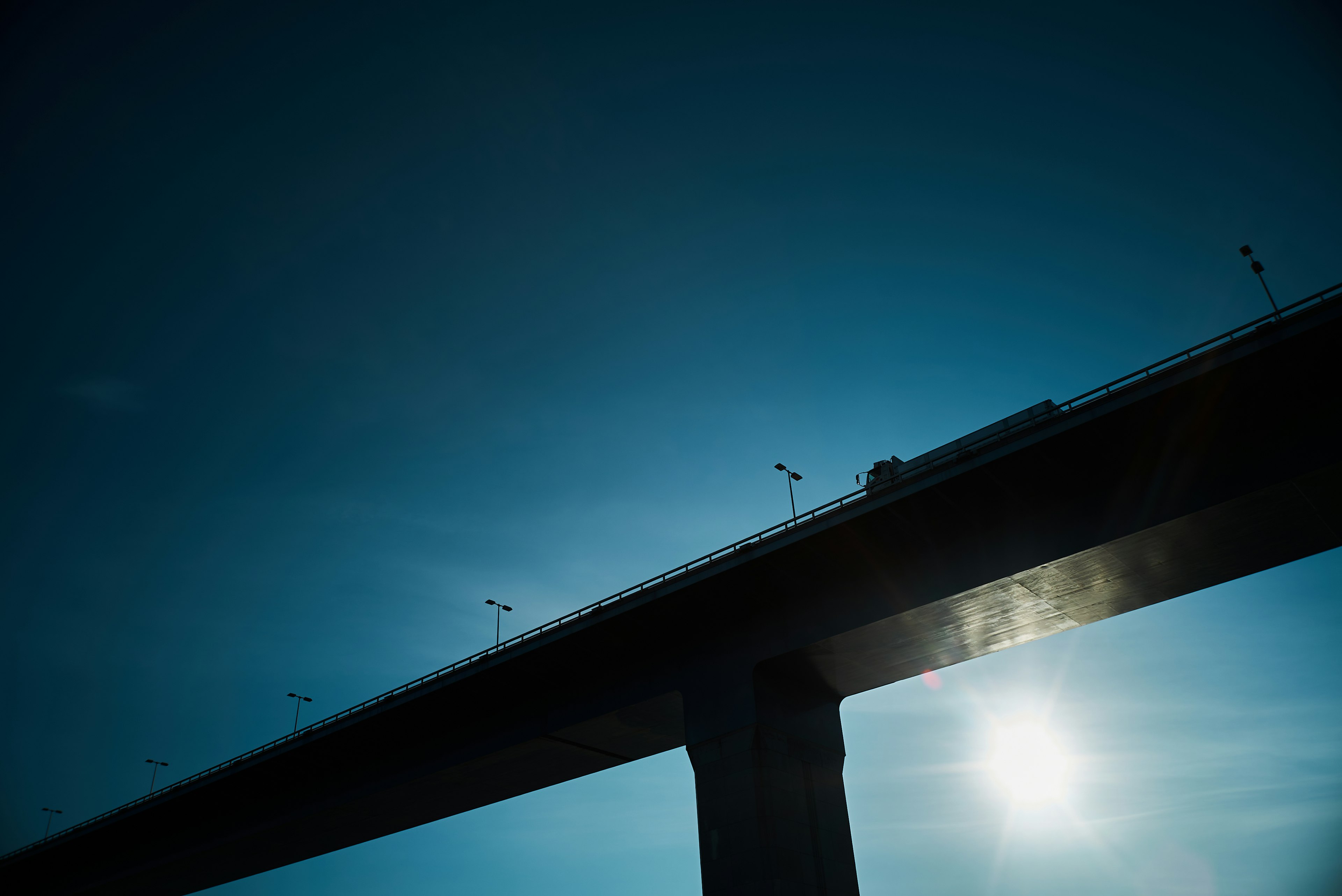 Siluet jembatan tinggi di bawah langit biru dan matahari