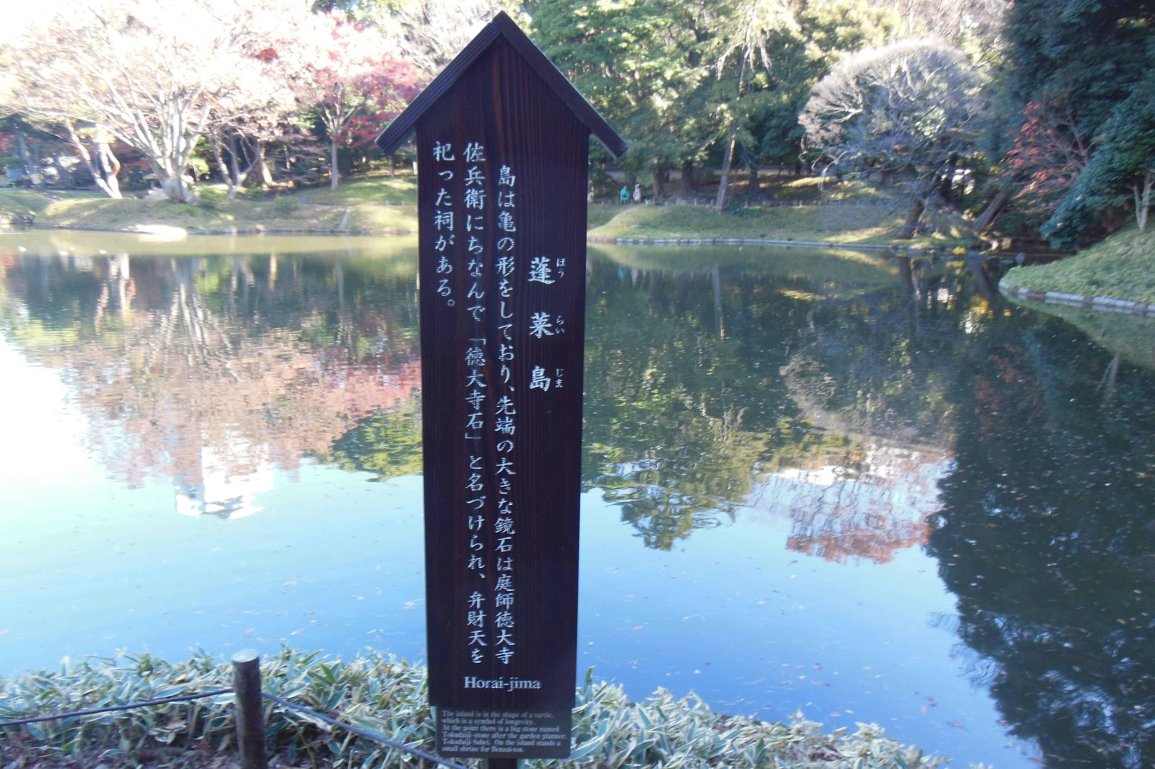 池の近くに立つ説明看板 緑の木々と静かな水面が映る