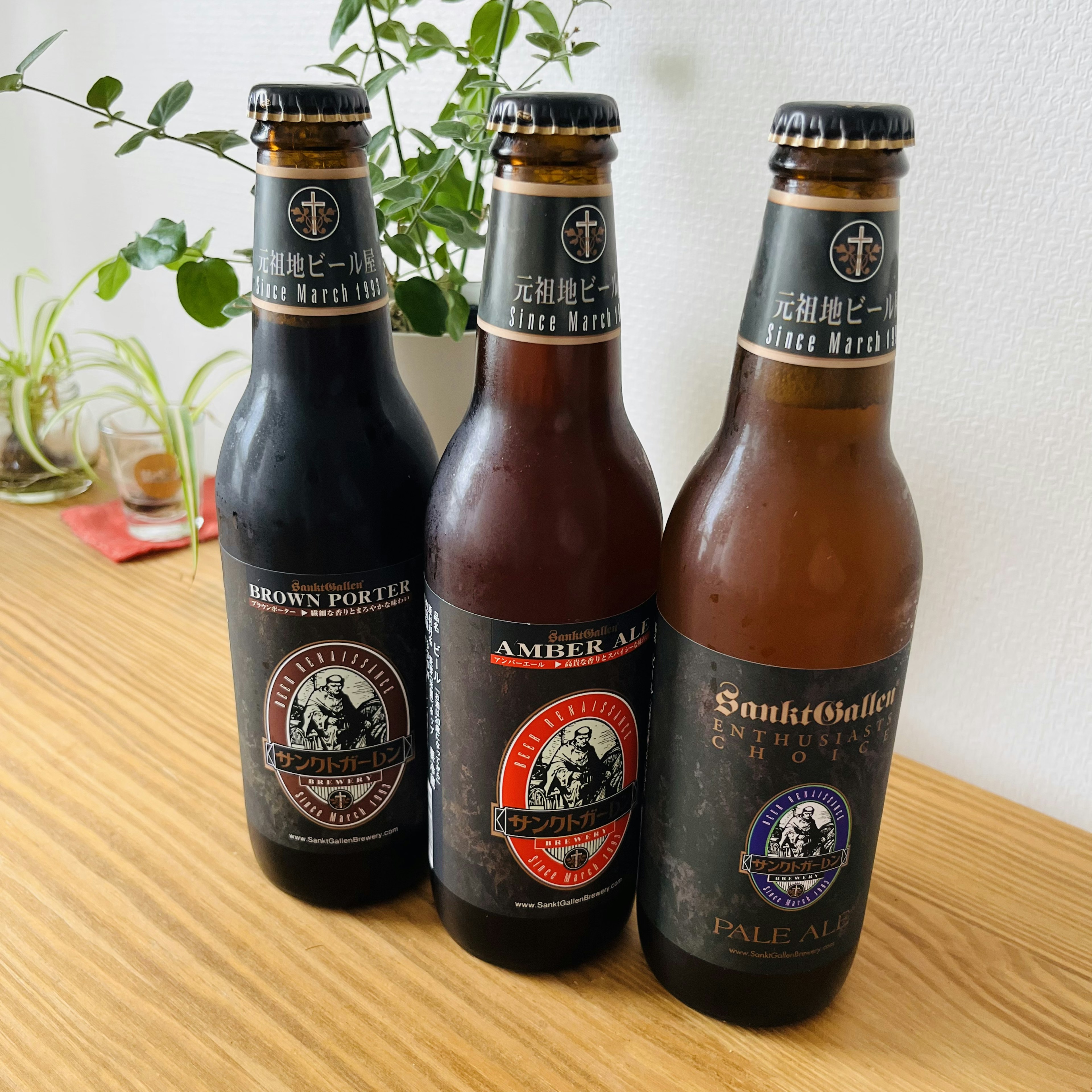 三本のビール瓶が木のテーブルに並んでいる黒いラベルのビールと琥珀色のビール