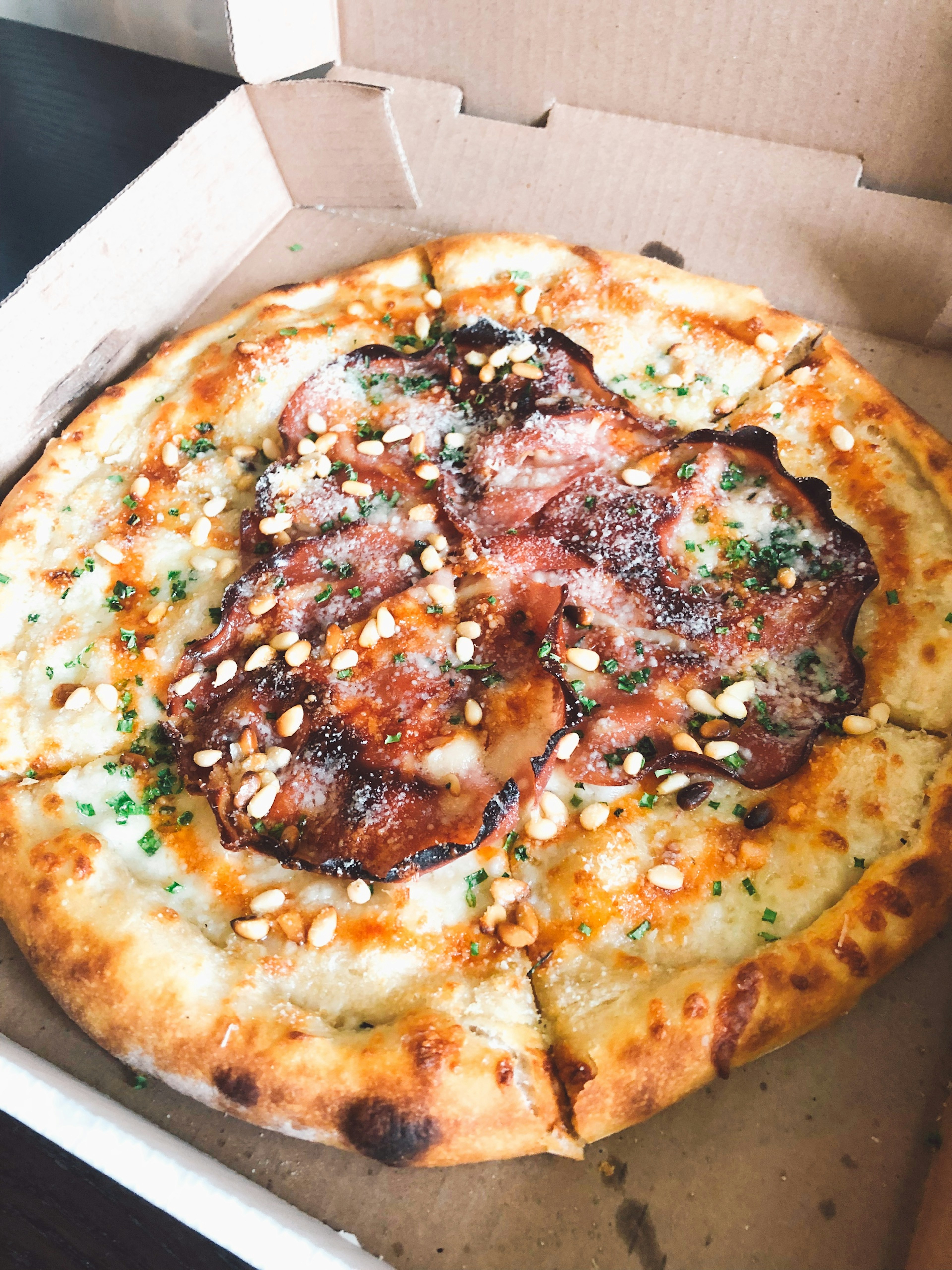 Pizza topped with cheese and nuts in a takeout box